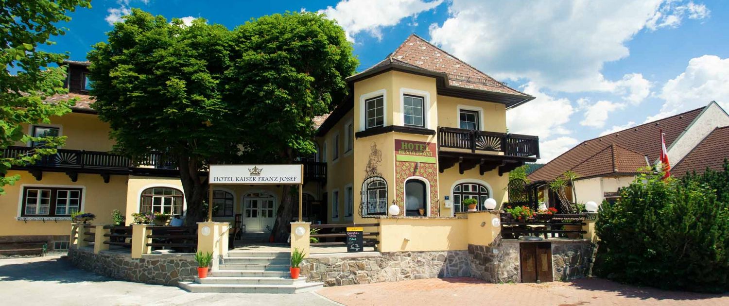 Eingang des Hotel Kaiser Franz Josef mit gelber Fassade und Balkon.