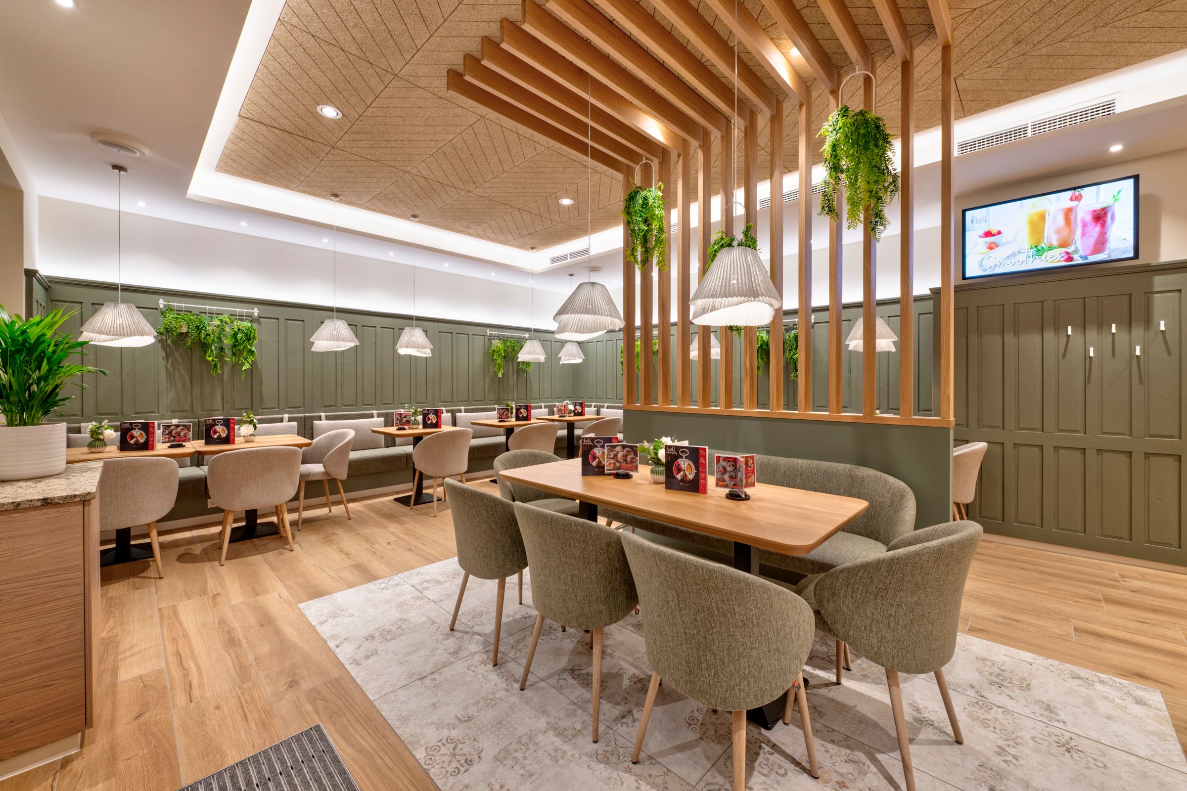 Innenansicht des modernen Cafés mit Holztischen, gepolsterten Stühlen und hängenden Pflanzen.