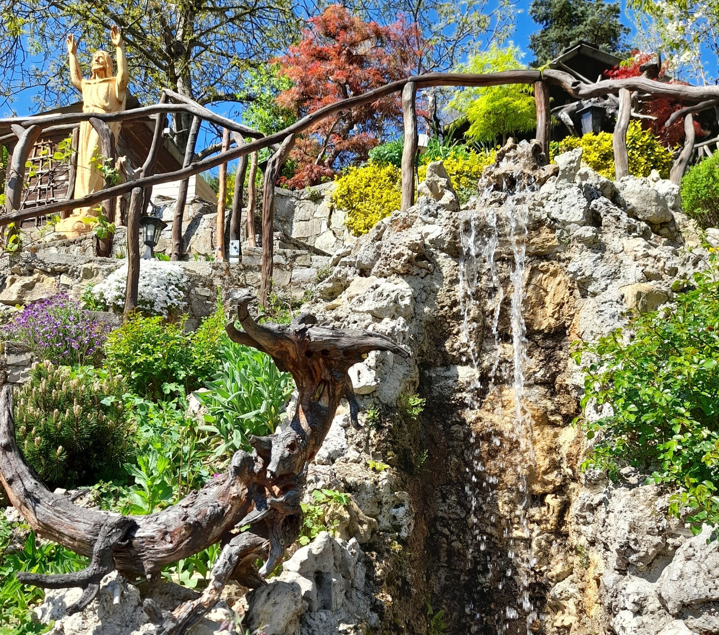 Garten mit Statue, Wasserfall und bunten Pflanzen.