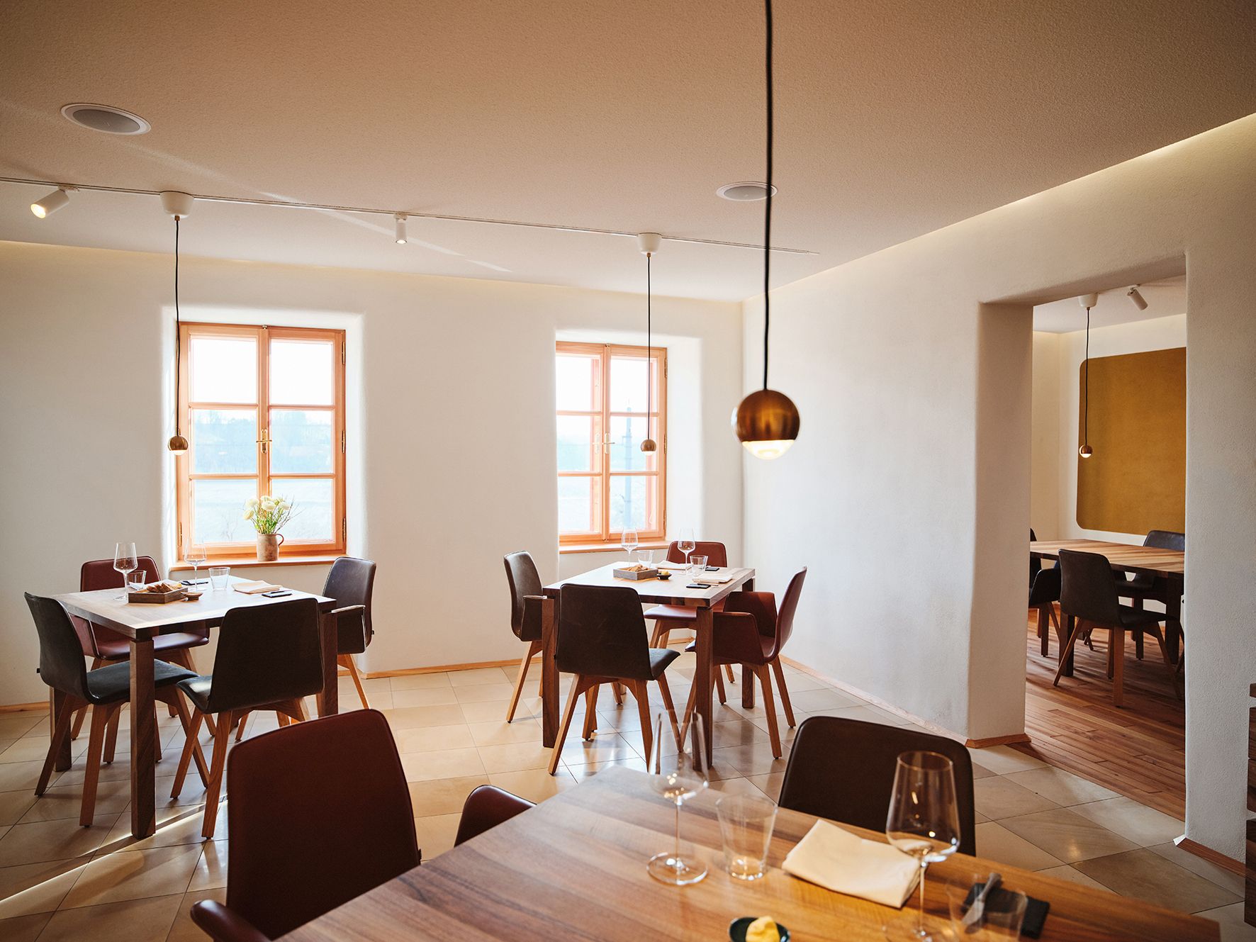 Moderner Gastraum mit Holztischen, Weingläsern und großen Fenstern im minimalistischen Design.