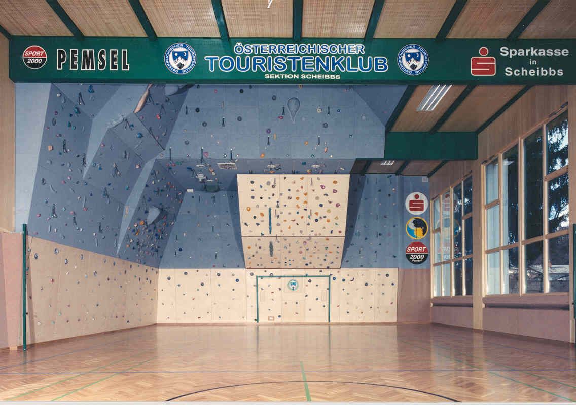 Innenansicht einer Kletterhalle mit blauer Kletterwand und bunten Griffen.