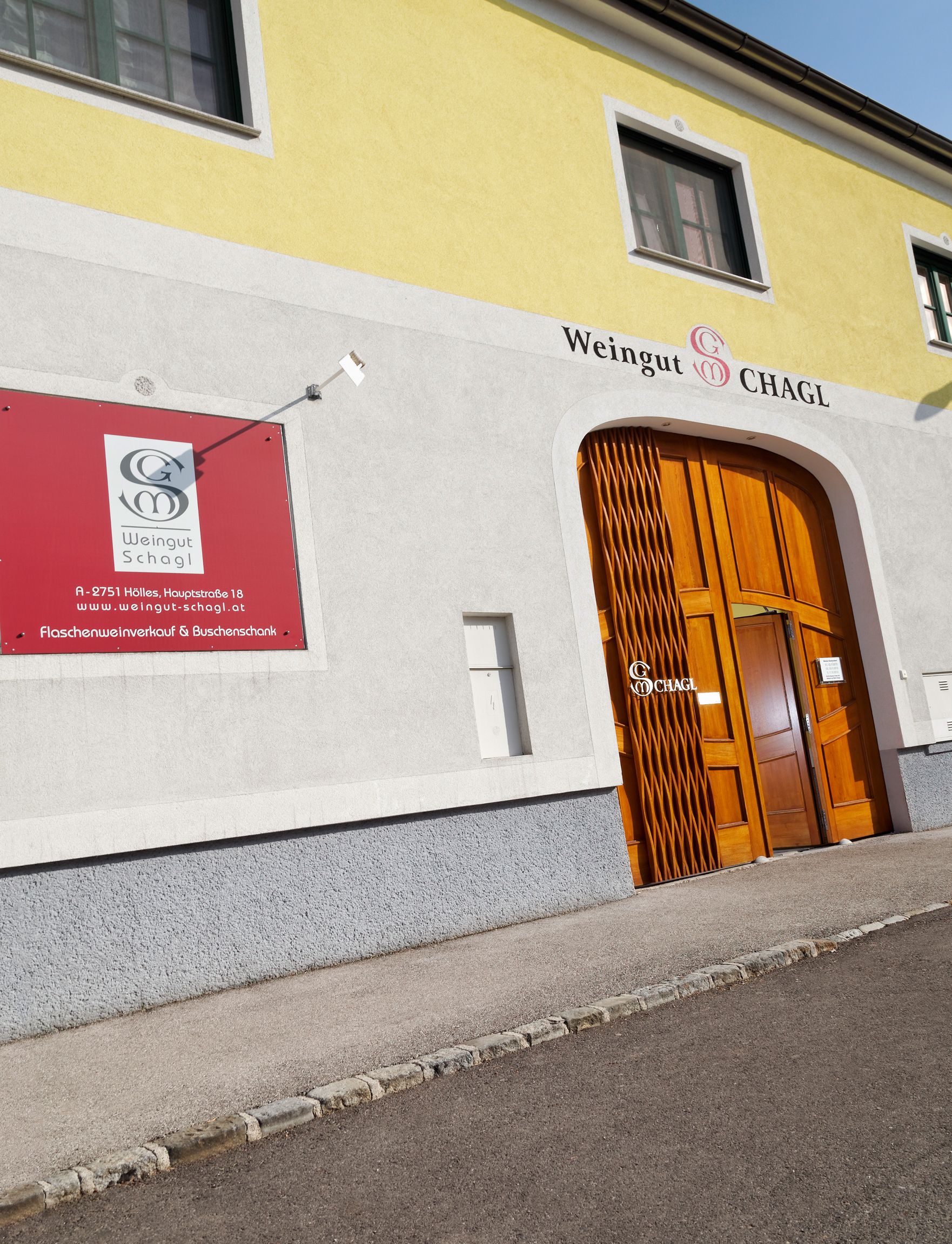 Eingang des Weinguts Schagl mit gelber Fassade und Holztür.