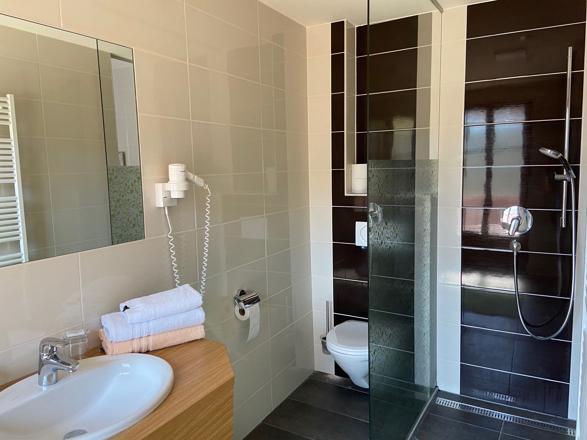 Modernes Badezimmer mit Waschbecken, Spiegel, Handtüchern, Toilette und Dusche.