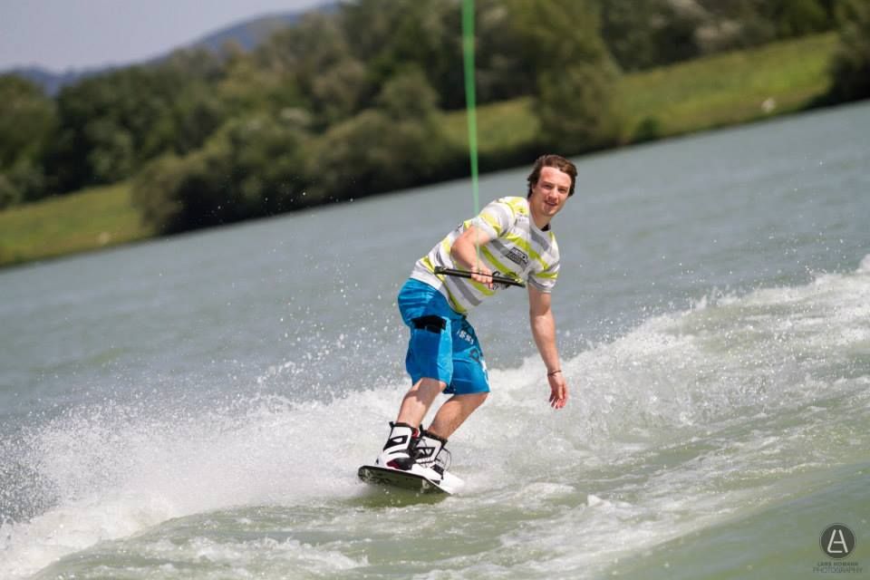 Ein Wakeboarder fährt auf einem See, umgeben von grüner Landschaft.
