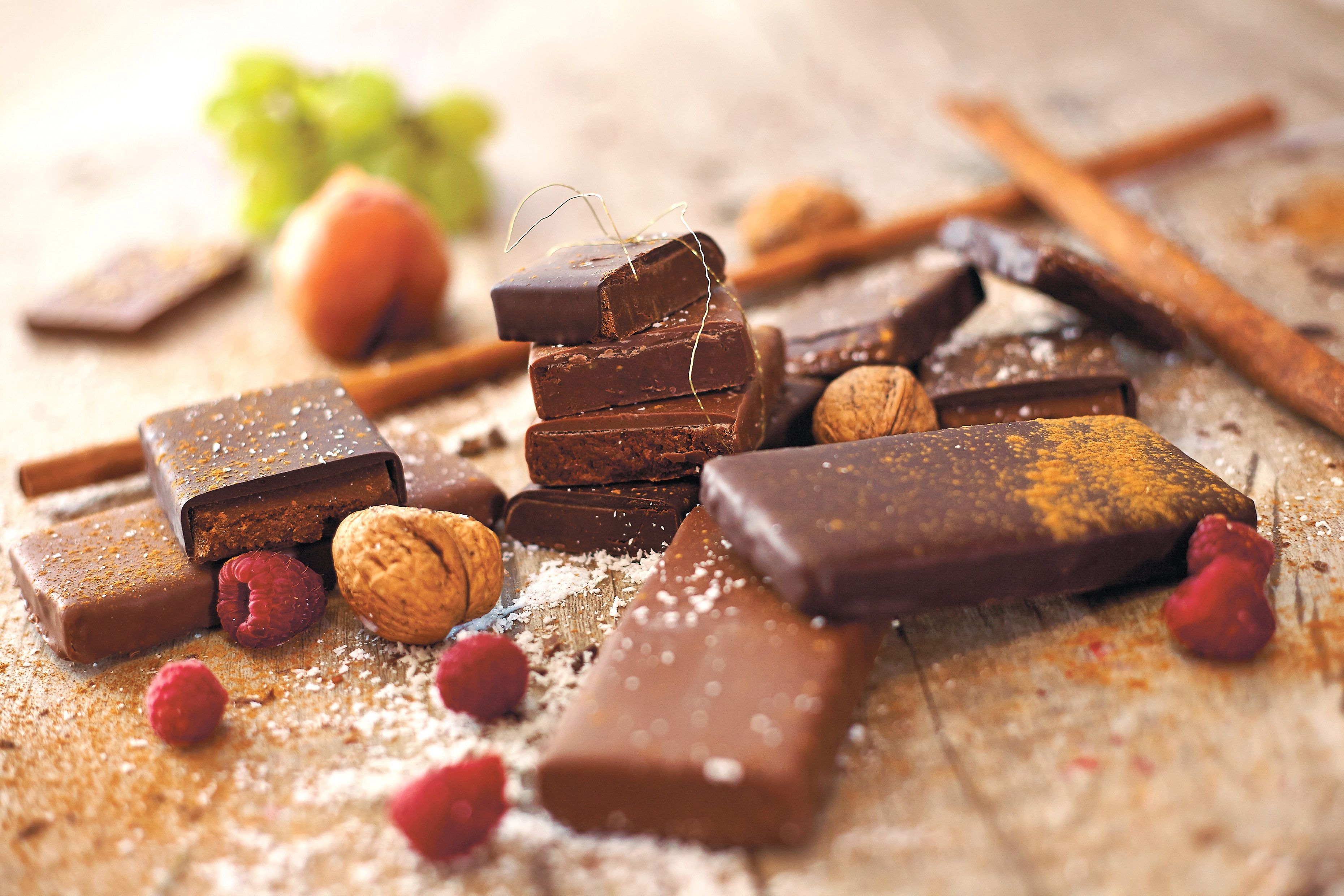 Verschiedene Schokoladenstücke mit Nüssen und Himbeeren auf einem Tisch.