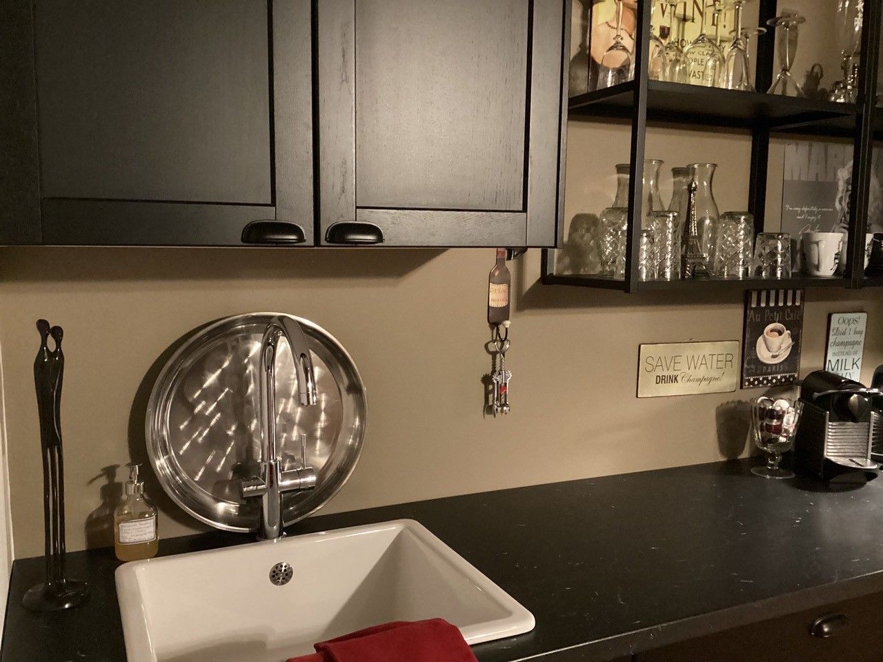 Moderne Küchenzeile mit Spüle, schwarzem Schrank, Regalen mit Gläsern und Kaffeemaschine.