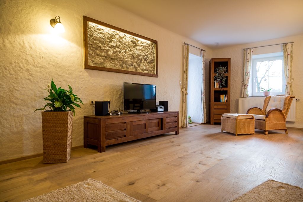 Gemütliches Wohnzimmer mit Holzmöbeln, Fernseher, Rattansessel und Pflanzen.