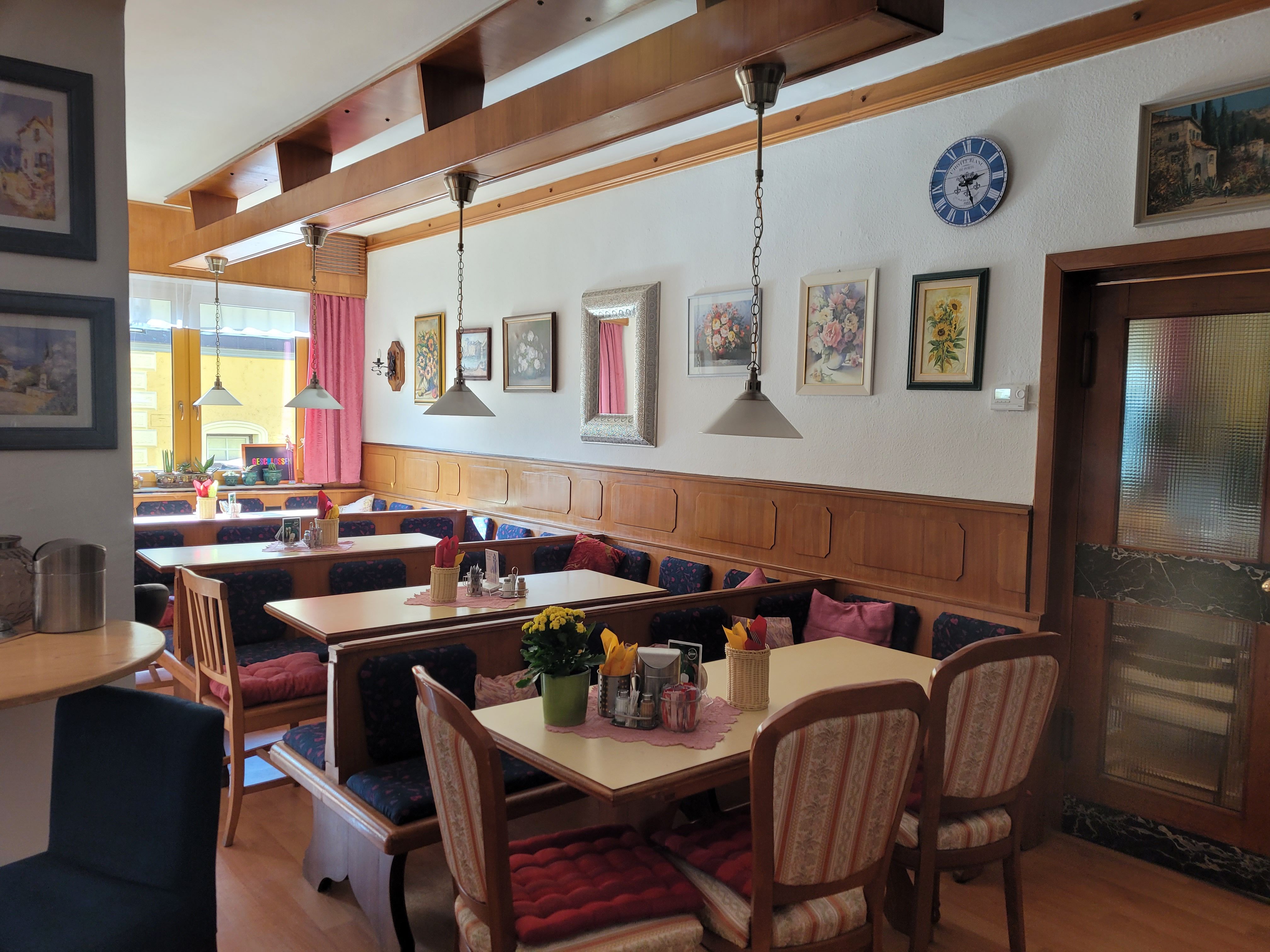 Gemütliche Gaststube mit Holzmöbeln, dekorativen Bildern an der Wand und gedeckten Tischen.