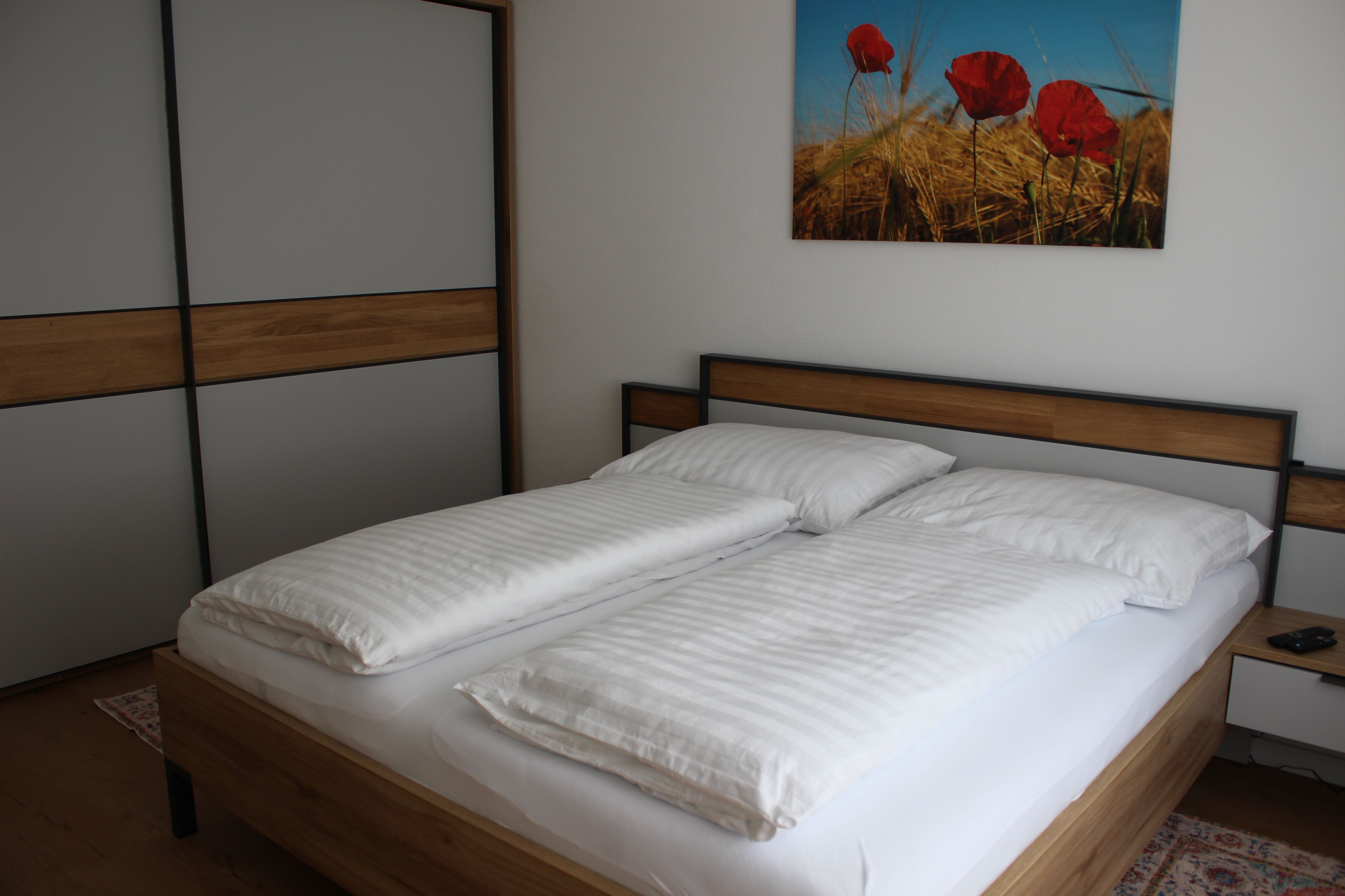 Ein modernes Schlafzimmer mit einem Doppelbett, weißen Bettbezügen und einem Bild von Mohnblumen an der Wand.