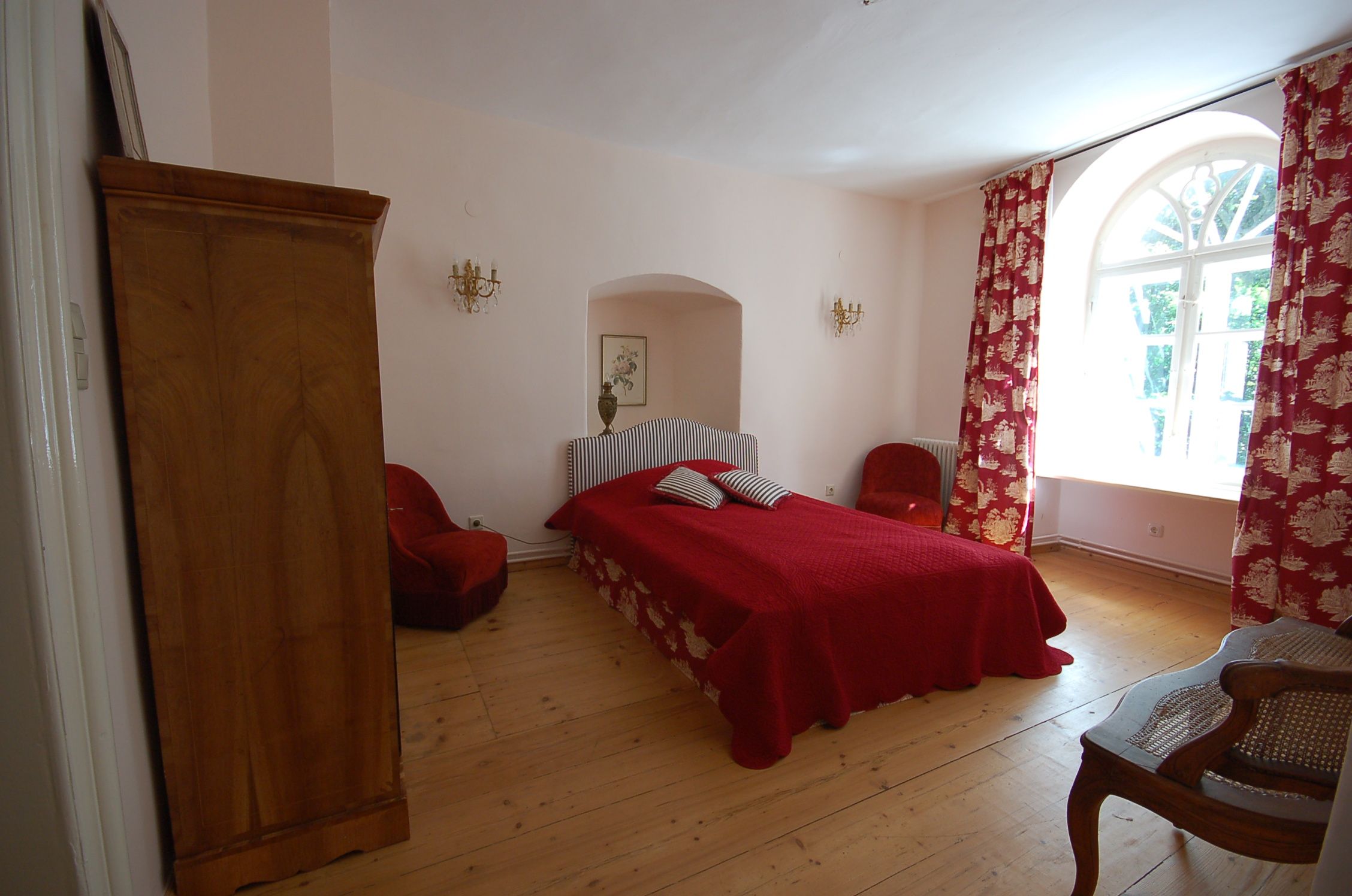 Ein gemütliches Schlafzimmer mit rotem Bett, roten Vorhängen und Holzmöbeln.