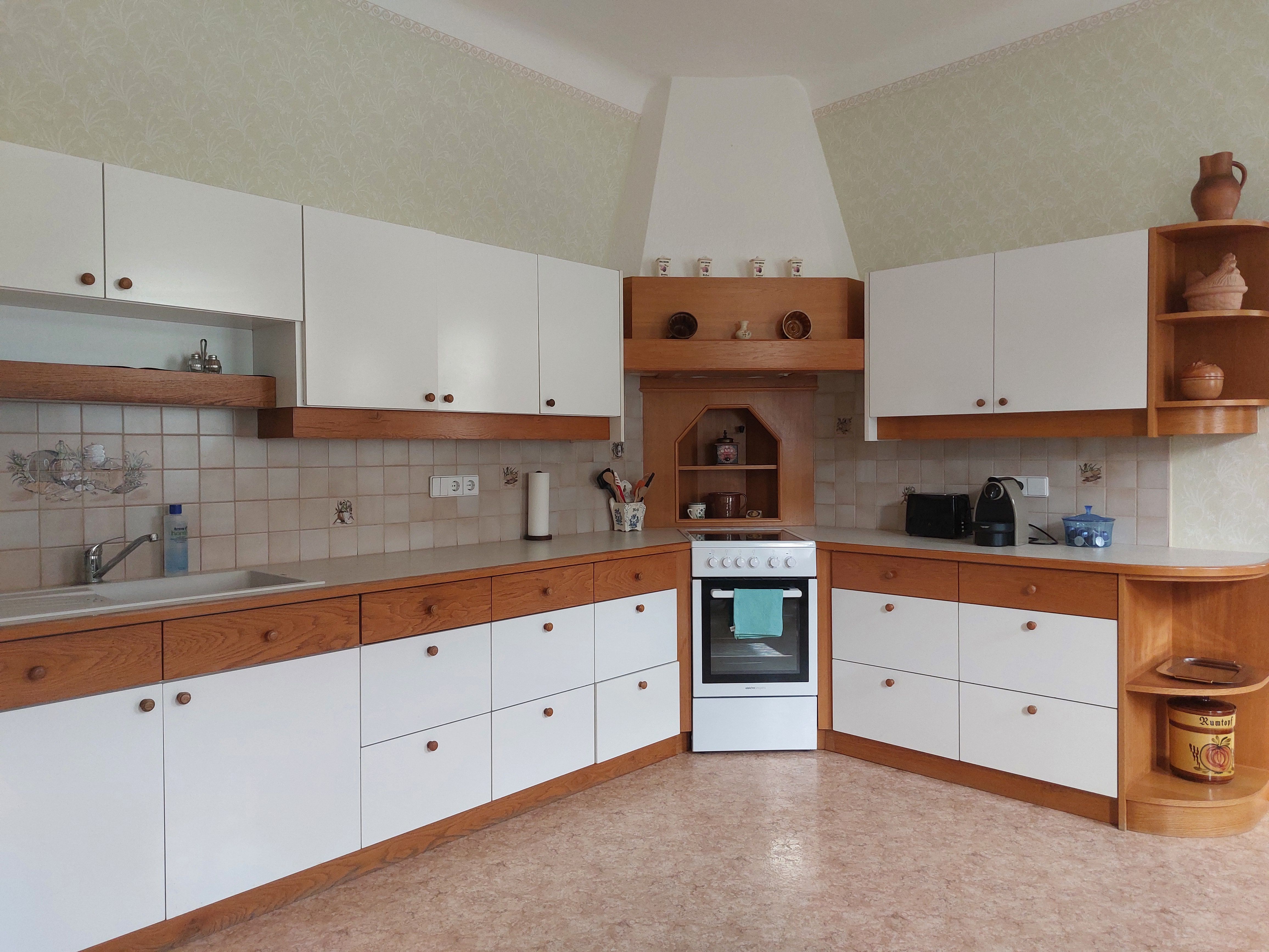 Küche mit weißen und holzfarbenen Schränken, Herd und Spüle.