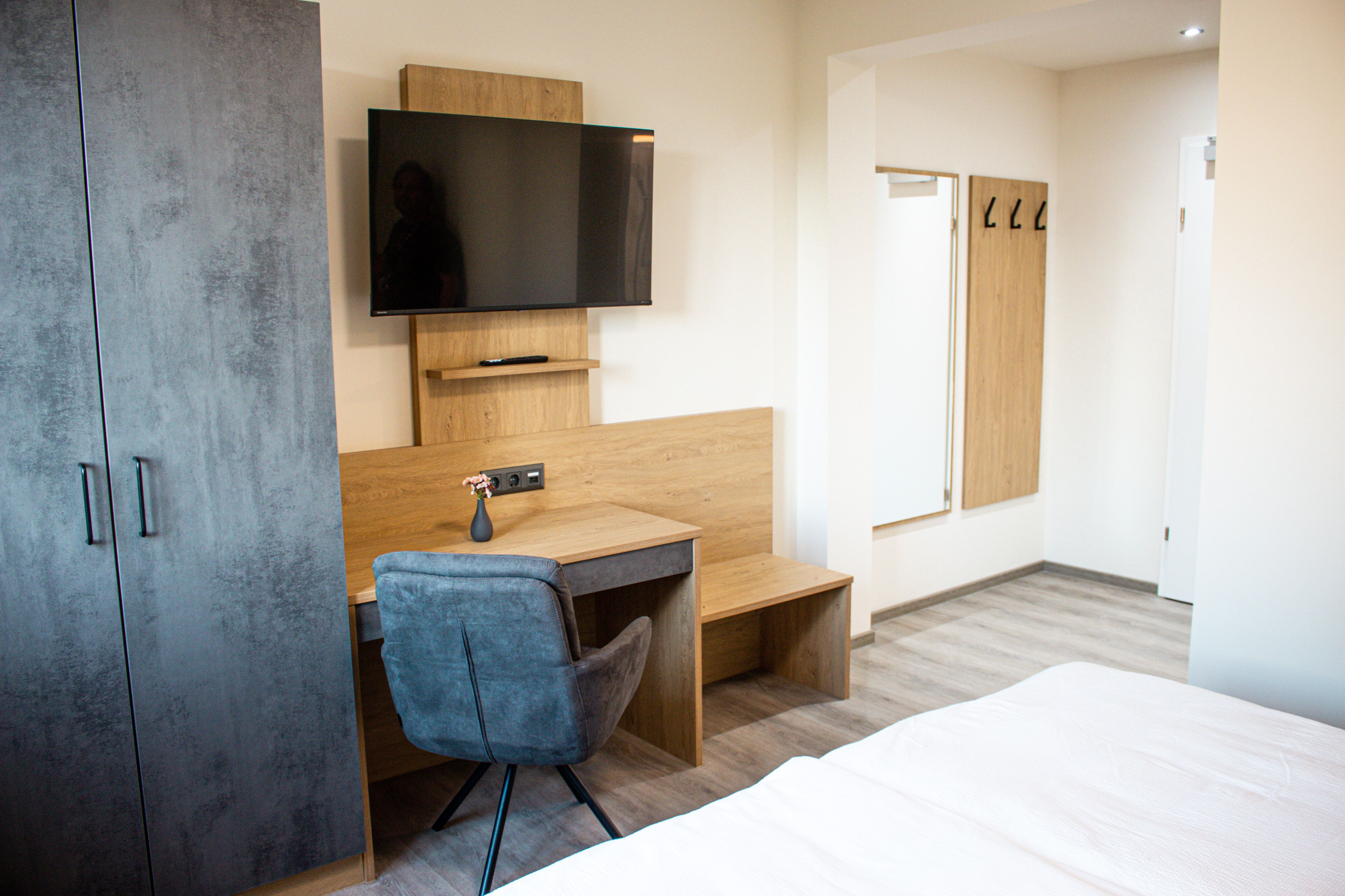 Modern eingerichtetes Hotelzimmer mit Schreibtisch, Fernseher, Kleiderschrank und Spiegel.