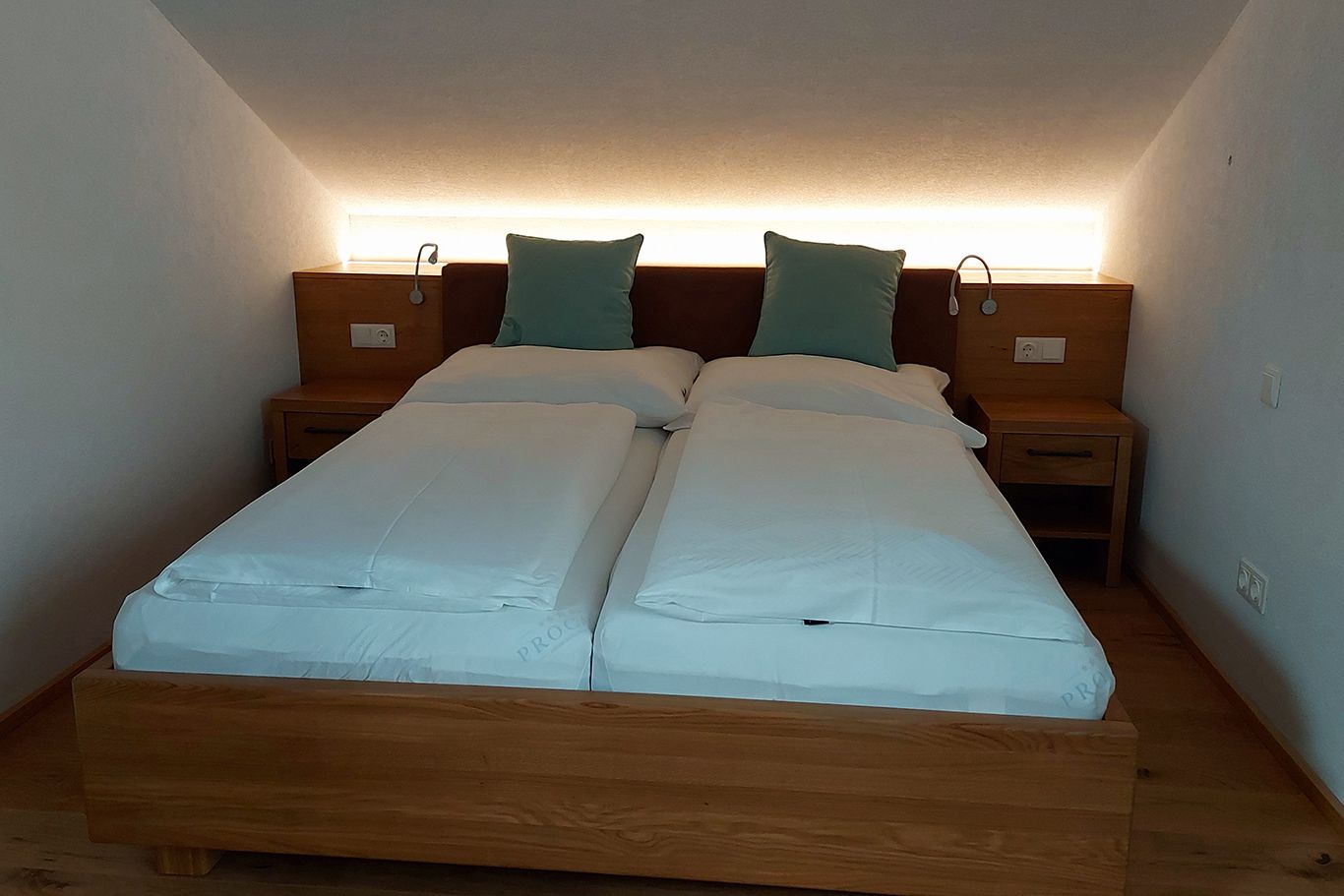 Ein Doppelbett in einem Zimmer mit schräger Decke, zwei Kissen und Nachttischen.