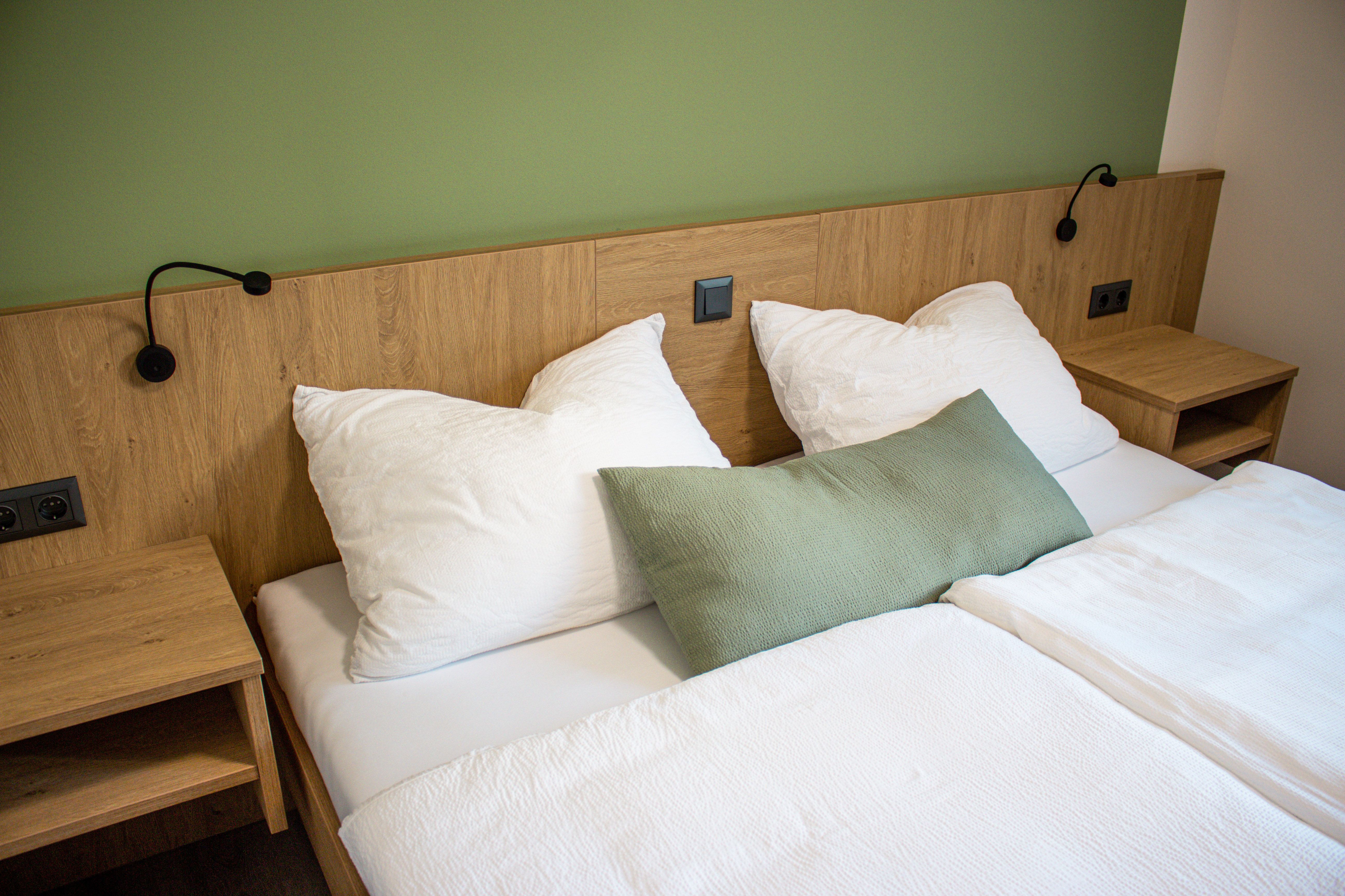 Ein Doppelbett mit weißer Bettwäsche und grüner Wand im Hintergrund.