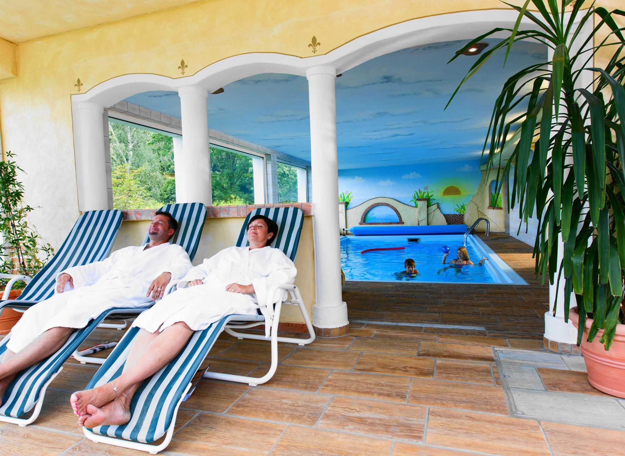 Zwei Personen entspannen auf Liegestühlen im Wellnessbereich neben einem Innenpool.
