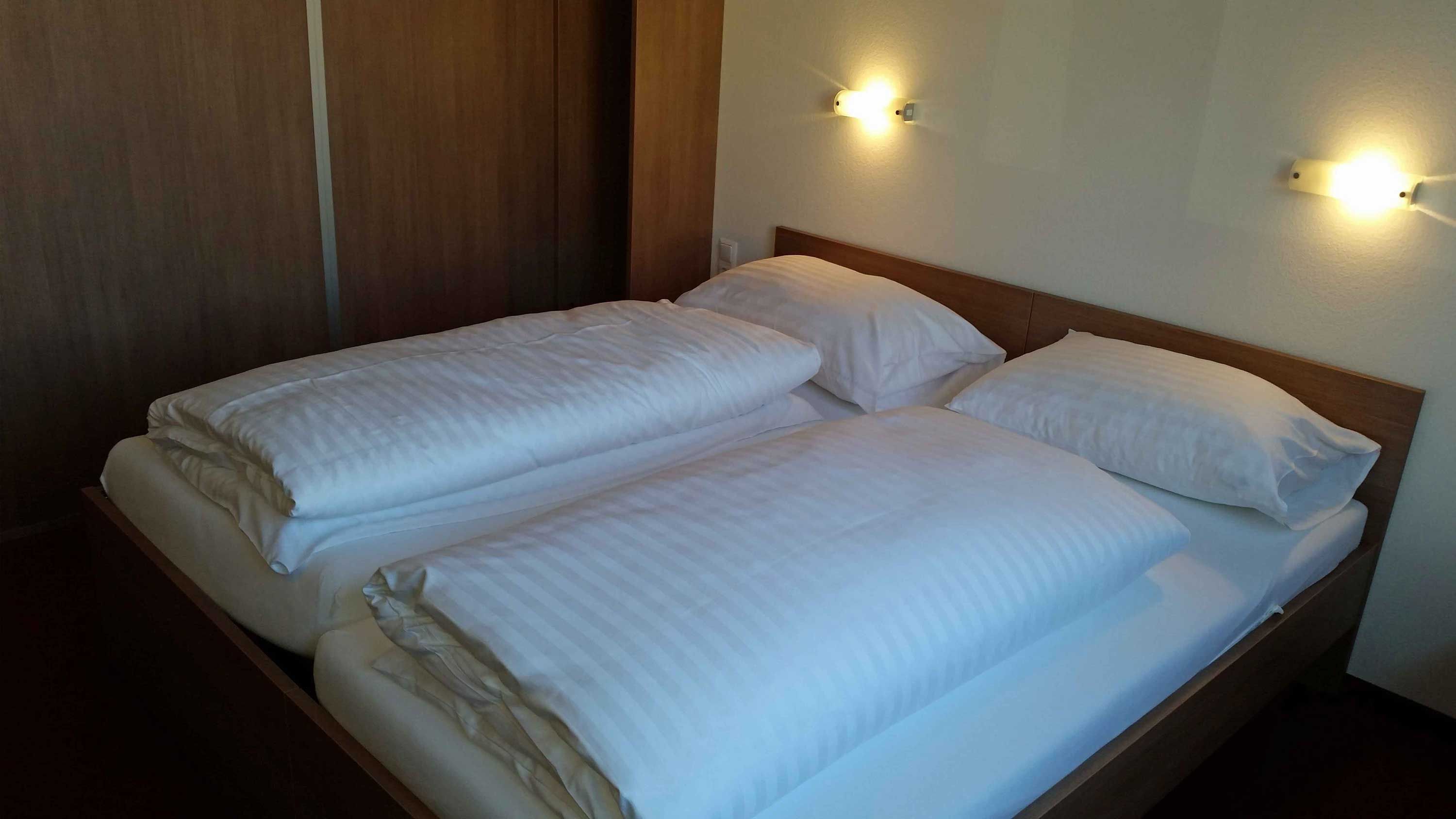 Ein Doppelbett in einem Motelzimmer mit weißen Bettdecken und Kissen, beleuchtet von zwei Wandlampen.