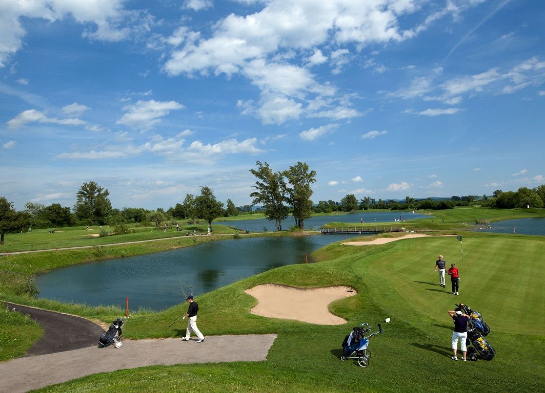 Golfplatz mit Wasserhindernissen und Spielern unter blauem Himmel.