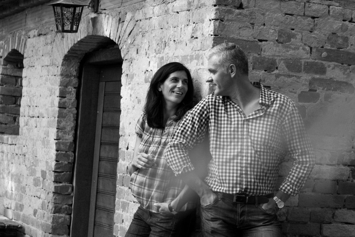 Ein Mann und eine Frau lehnen lächelnd an einer Backsteinmauer.