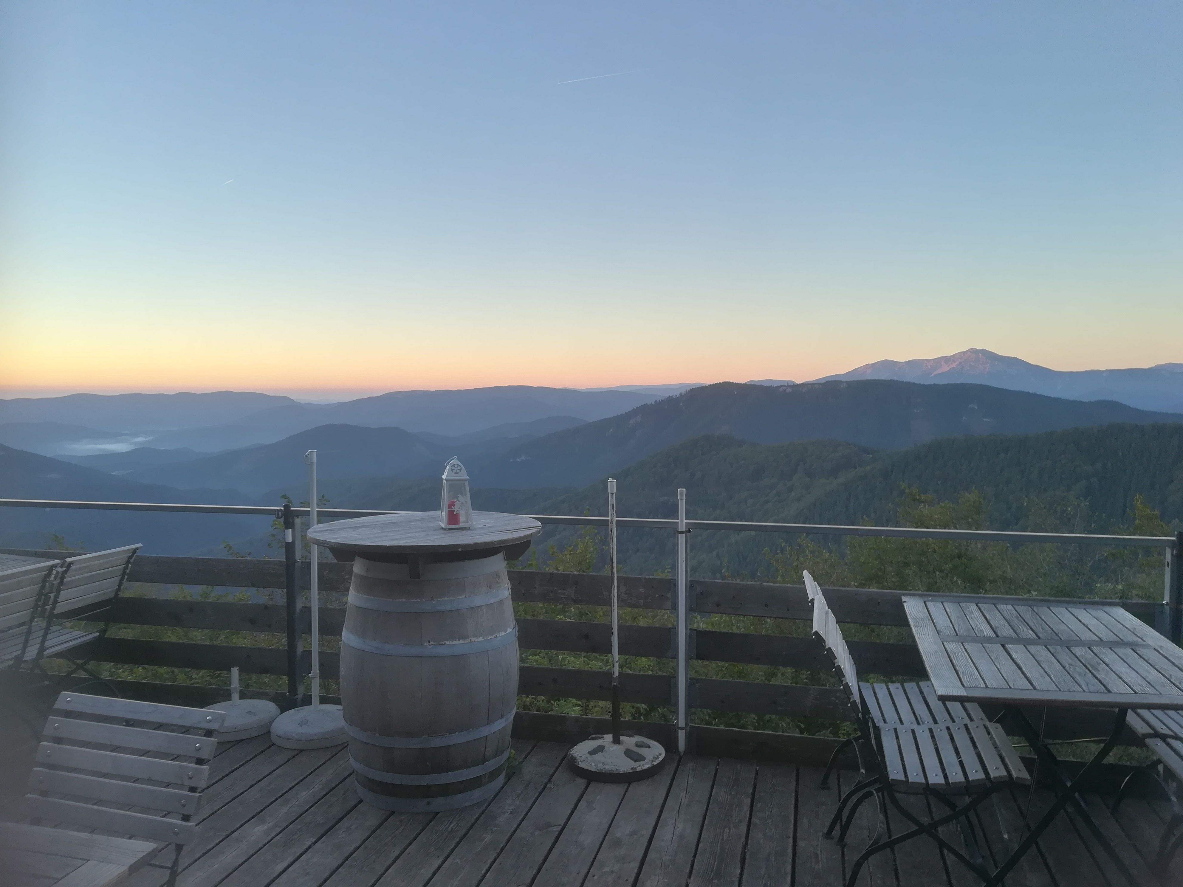 Terrasse mit Holzmöbeln und Bergblick bei Sonnenaufgang.
