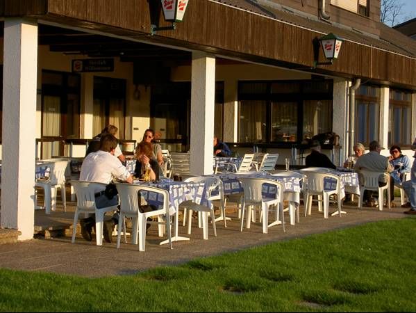 Menschen sitzen an Tischen im Freien vor einem Gebäude.