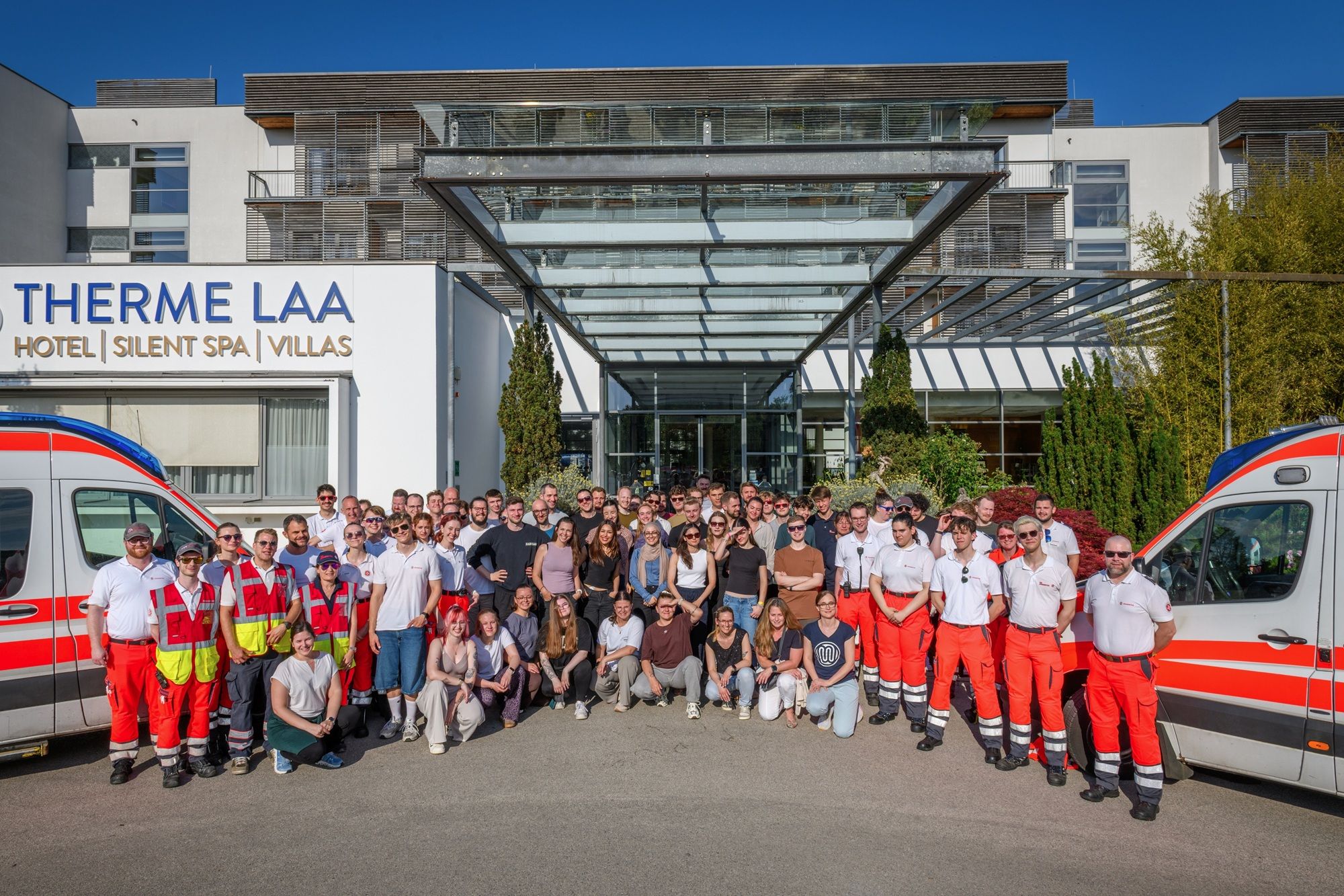 Eine Gruppe von Seminarteilnehmer:innen sthehen neben einem Rettungsauto vor dem Eingang des Hotels Therme Laa