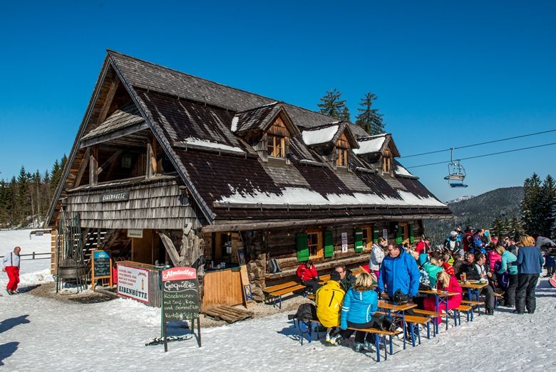 Eine Berghütte im Schnee mit Menschen, die draußen sitzen.