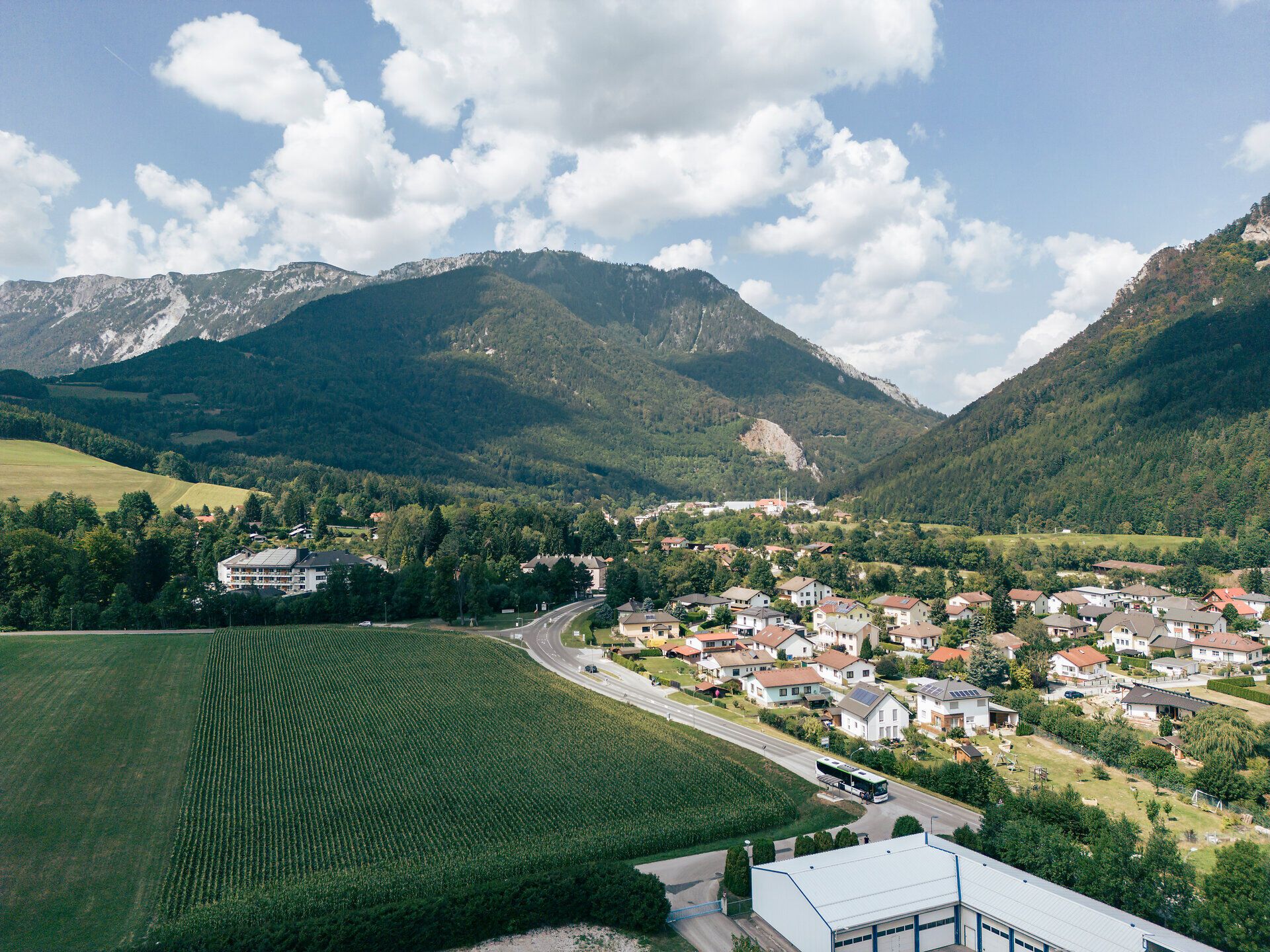 Blick über ein alpines Tal mit Dorf, Feldern und Bergen unter blauem Himmel.