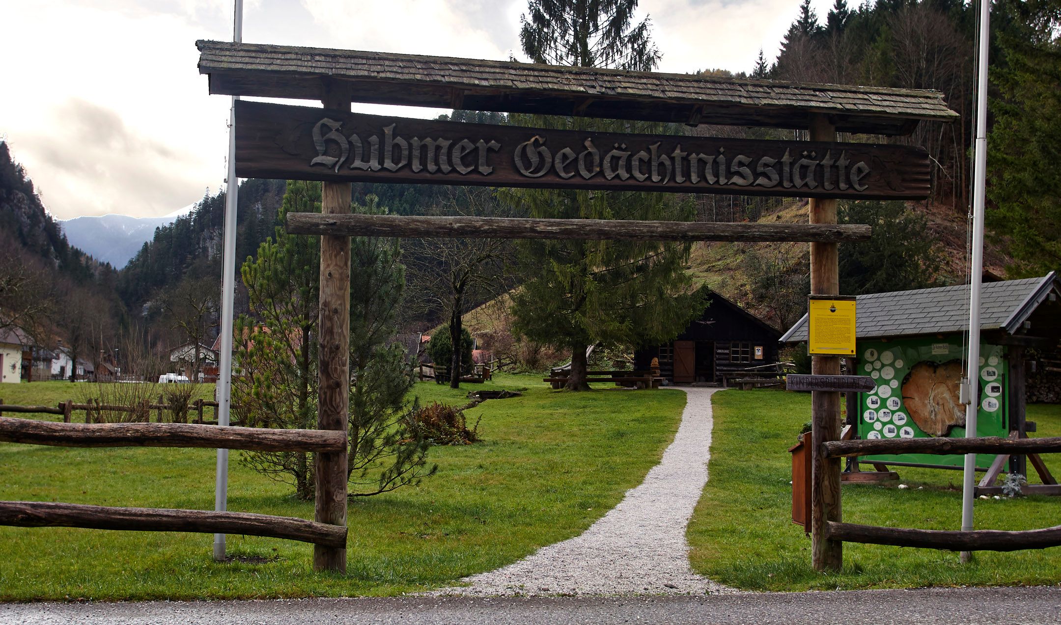 Eingang zur Hubmer Gedächtnisstätte mit Holztor und Weg.