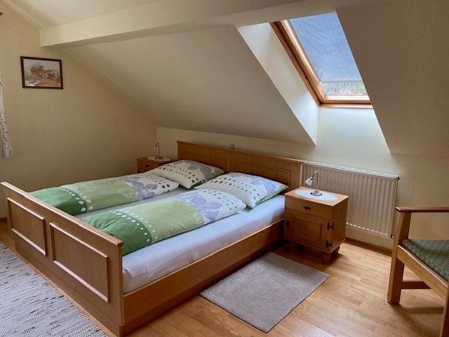 Gemütliches Doppelzimmer mit Dachfenster, Holzbett und Nachttisch.