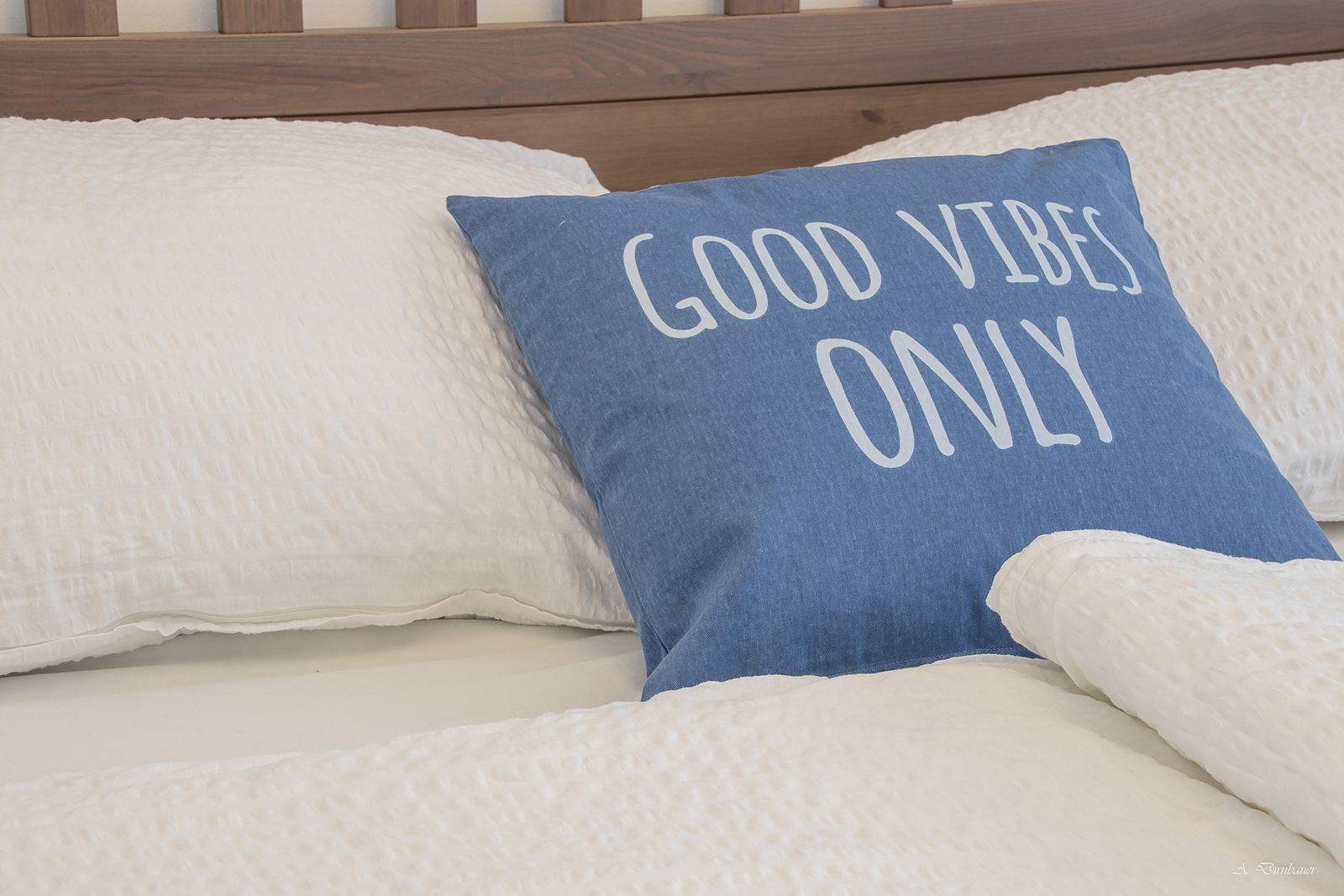 Bett mit blauem Kissen, Aufschrift 'Good Vibes Only'.
