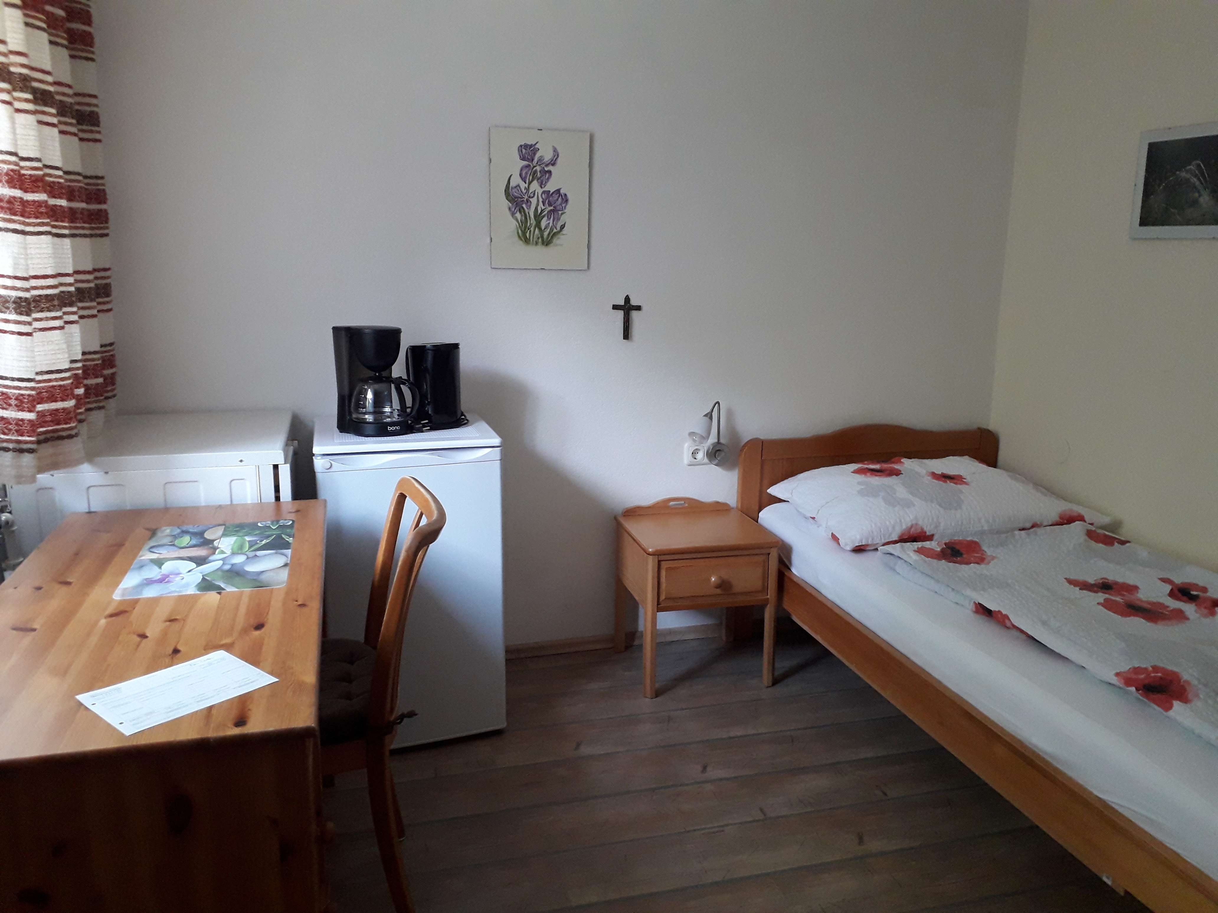 Ein einfach eingerichtetes Zimmer mit Bett, Tisch, Stuhl, Kühlschrank und Kaffeemaschine.