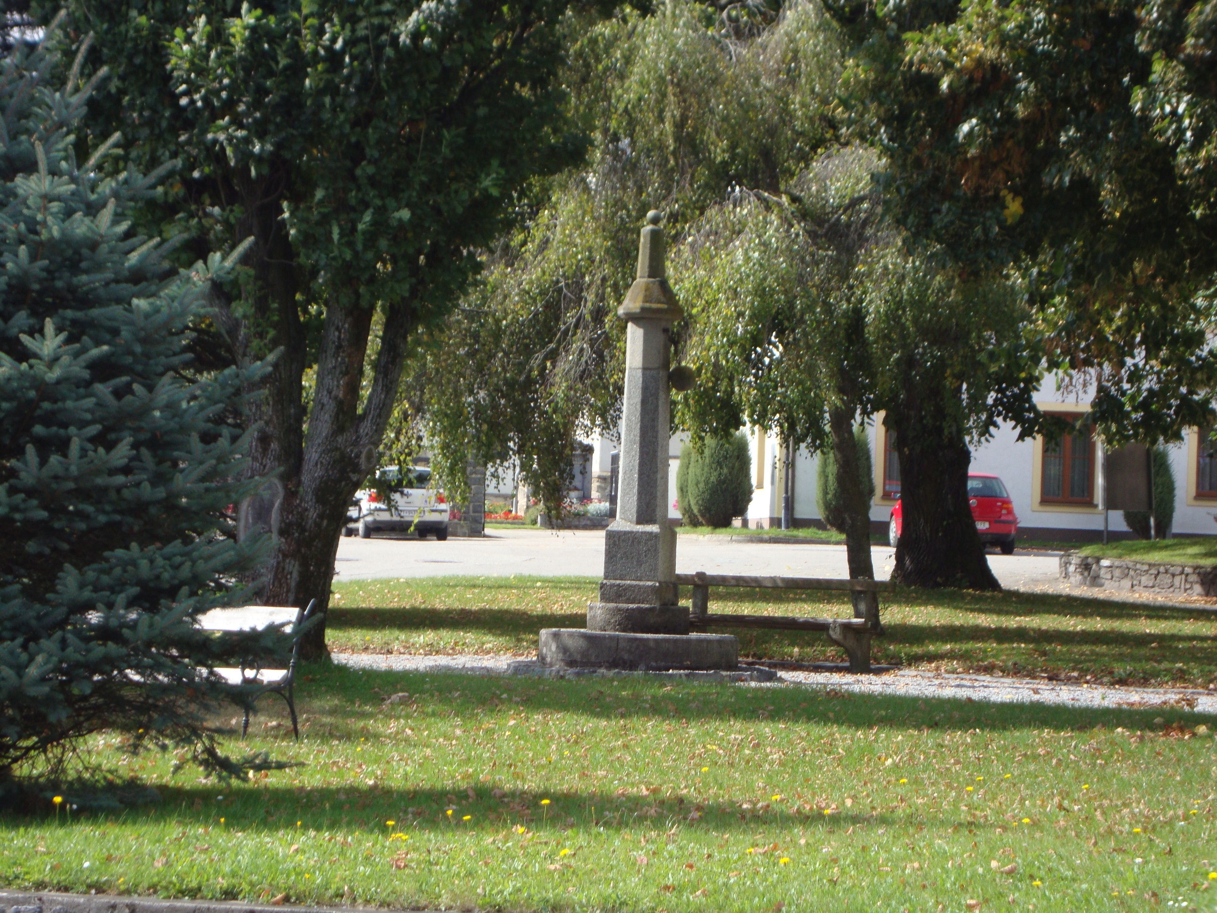 Ein kleiner Park mit einem steinernen Denkmal und einer Bank, umgeben von Bäumen.