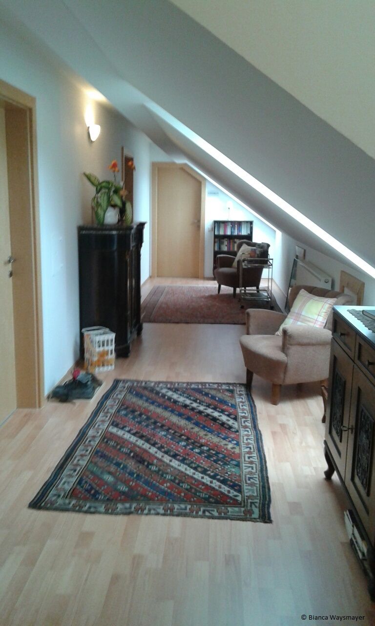 Ein gemütlicher Dachgeschossflur mit Teppich, Pflanzen und Möbeln.