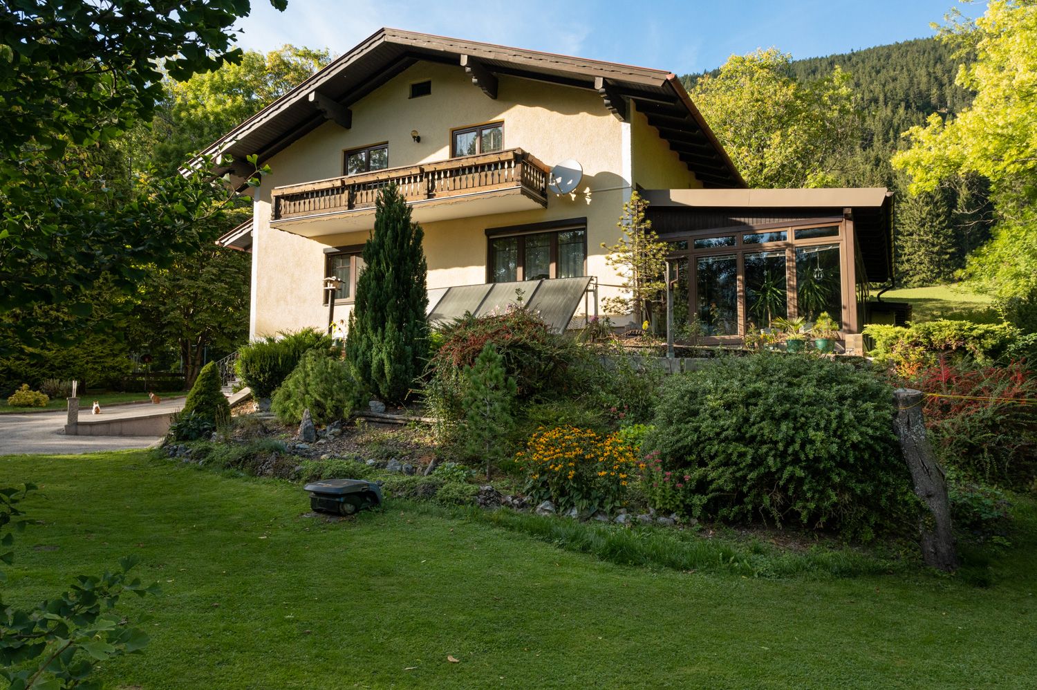 Ein zweistöckiges Ferienhaus mit Balkon und Garten, umgeben von Bäumen und Wiese.