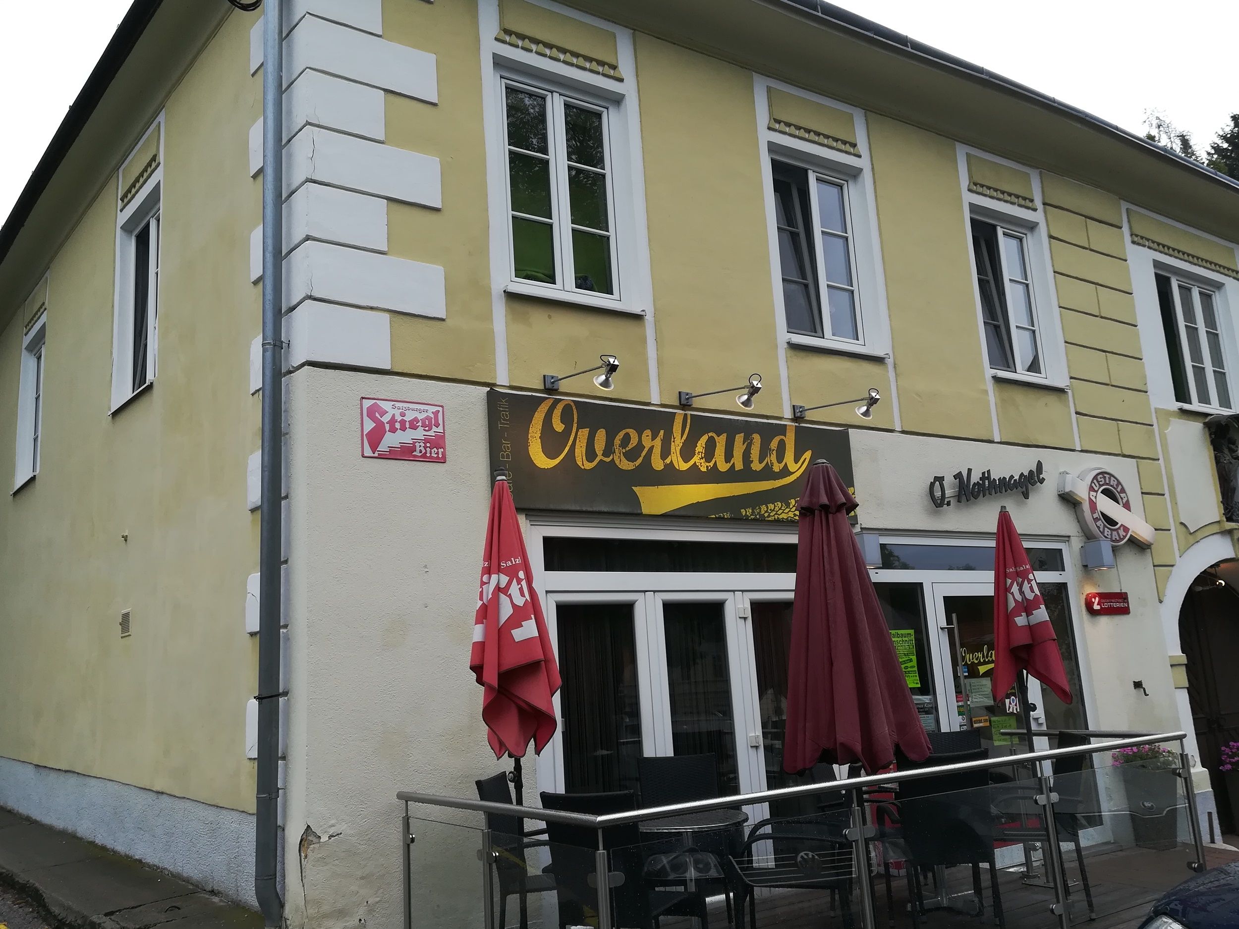 Gelbes Gebäude mit dem Schriftzug 'Overland' und roten Sonnenschirmen.