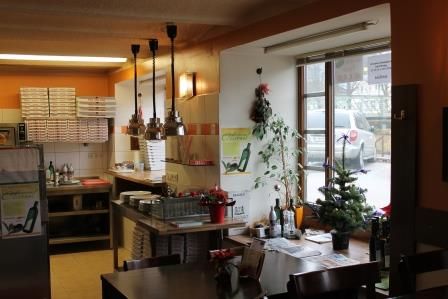 Innenansicht einer Pizzeria mit Tischen, Stühlen und Dekorationen.