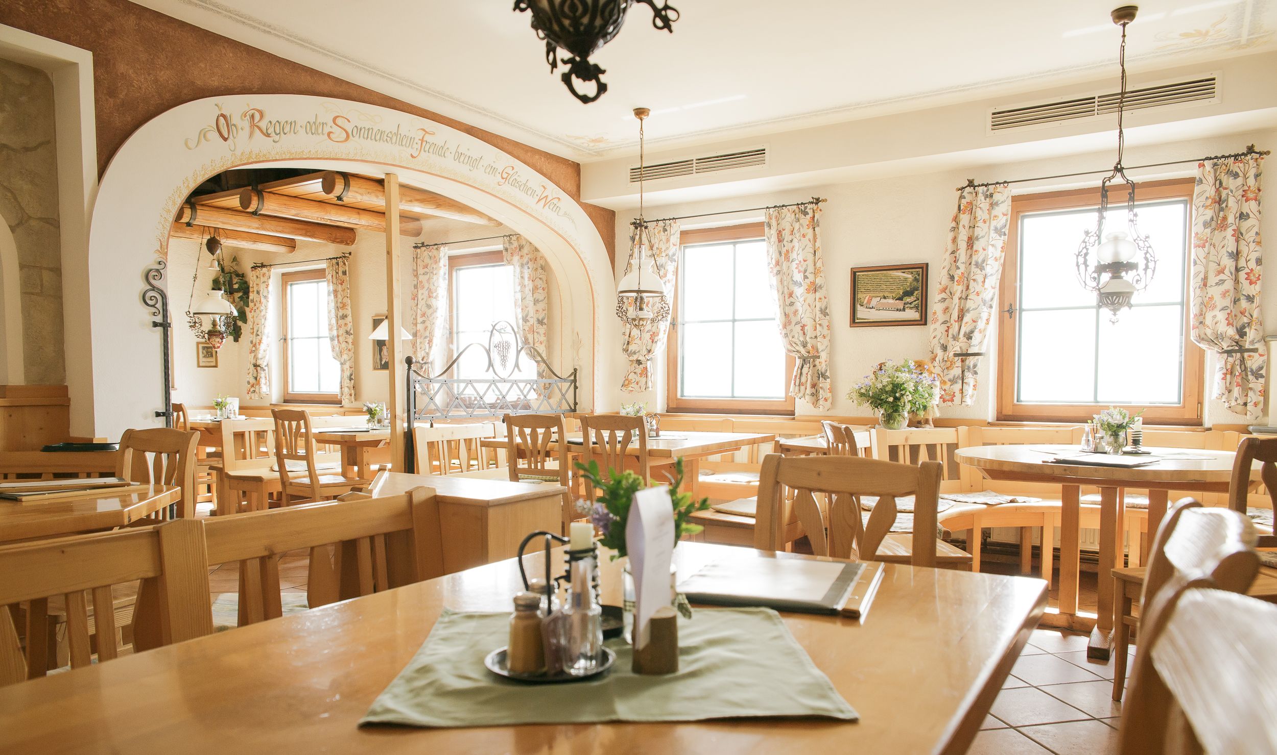 Innenansicht eines gemütlichen Restaurants mit Holzmöbeln und floralen Vorhängen.