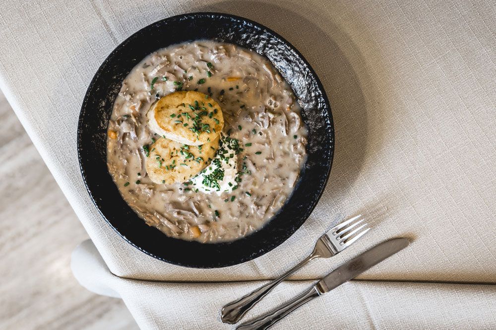 Ein Teller mit Beuschl und zwei Semmelknödeln, garniert mit Schnittlauch, auf einem Tisch mit Besteck.