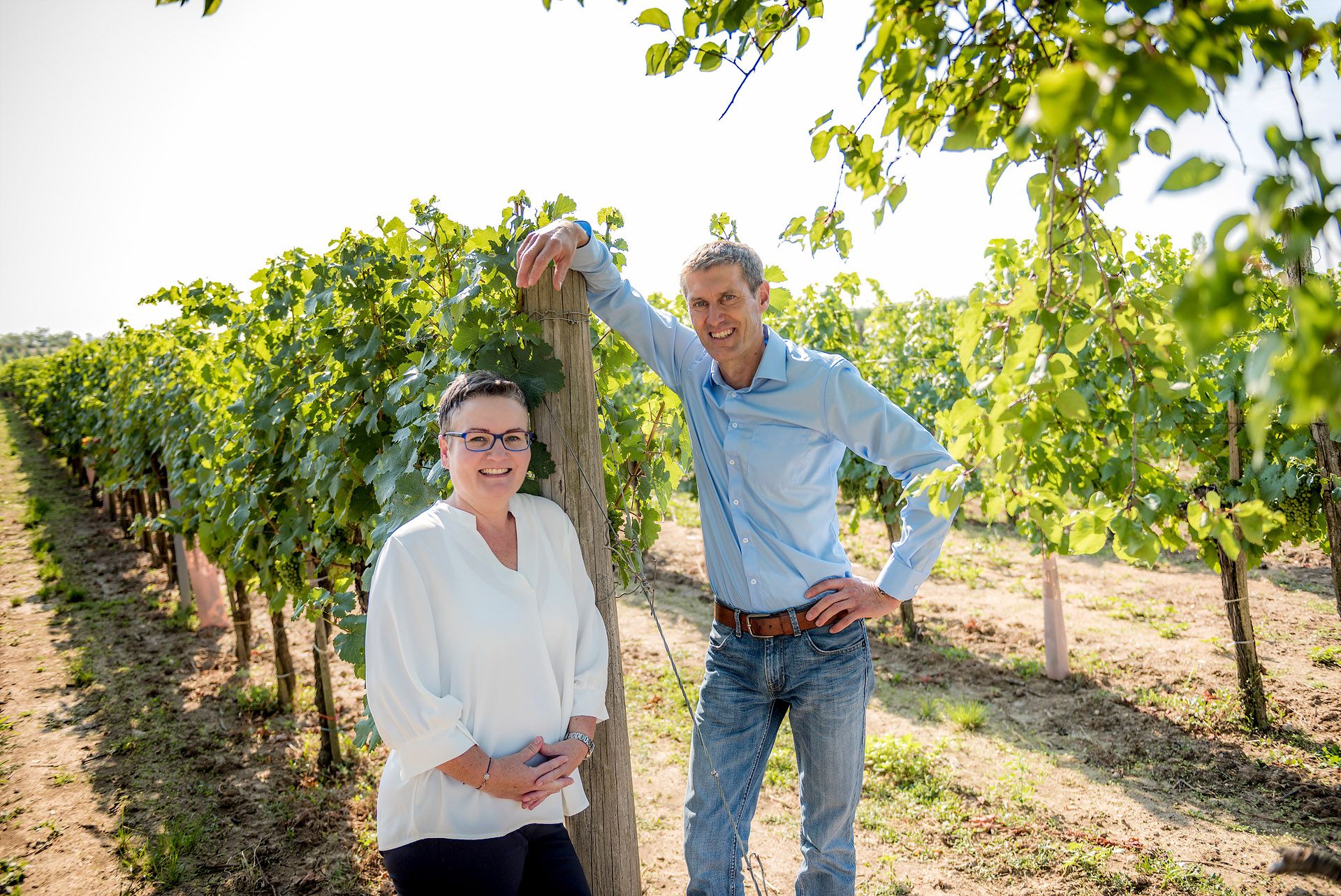Ein Mann und eine Frau stehen lächelnd in einem Weinberg.
