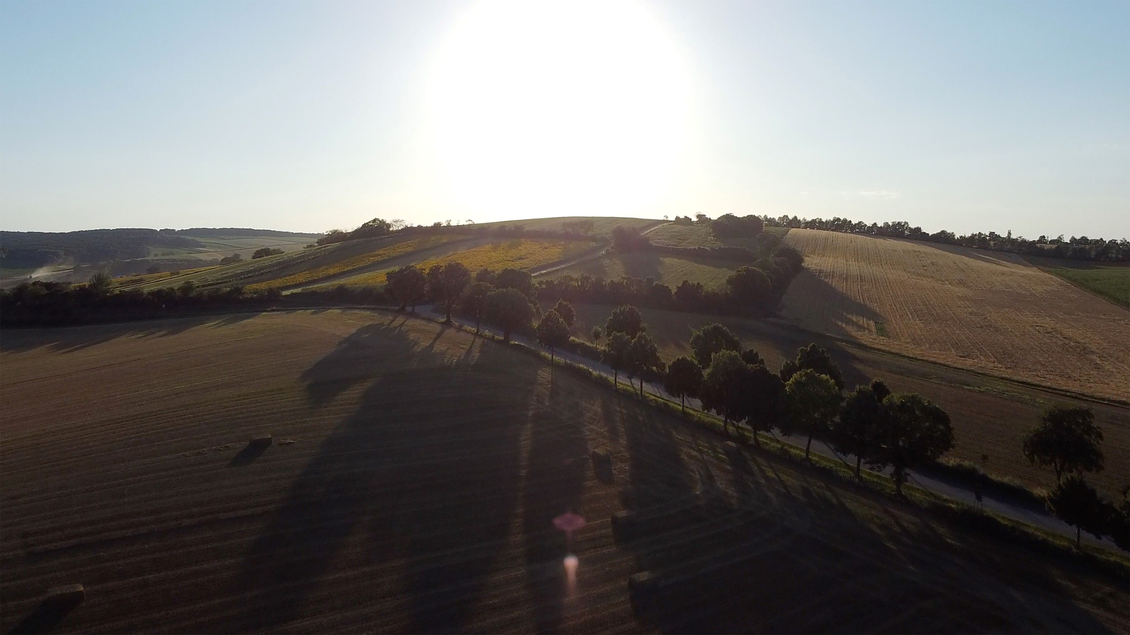 Sonnenuntergang über einer hügeligen Landschaft mit Feldern und Bäumen.