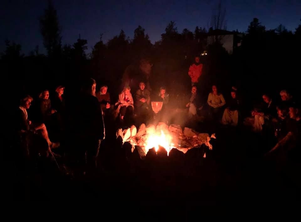 Menschen sitzen im Kreis um ein Lagerfeuer in der Nacht.