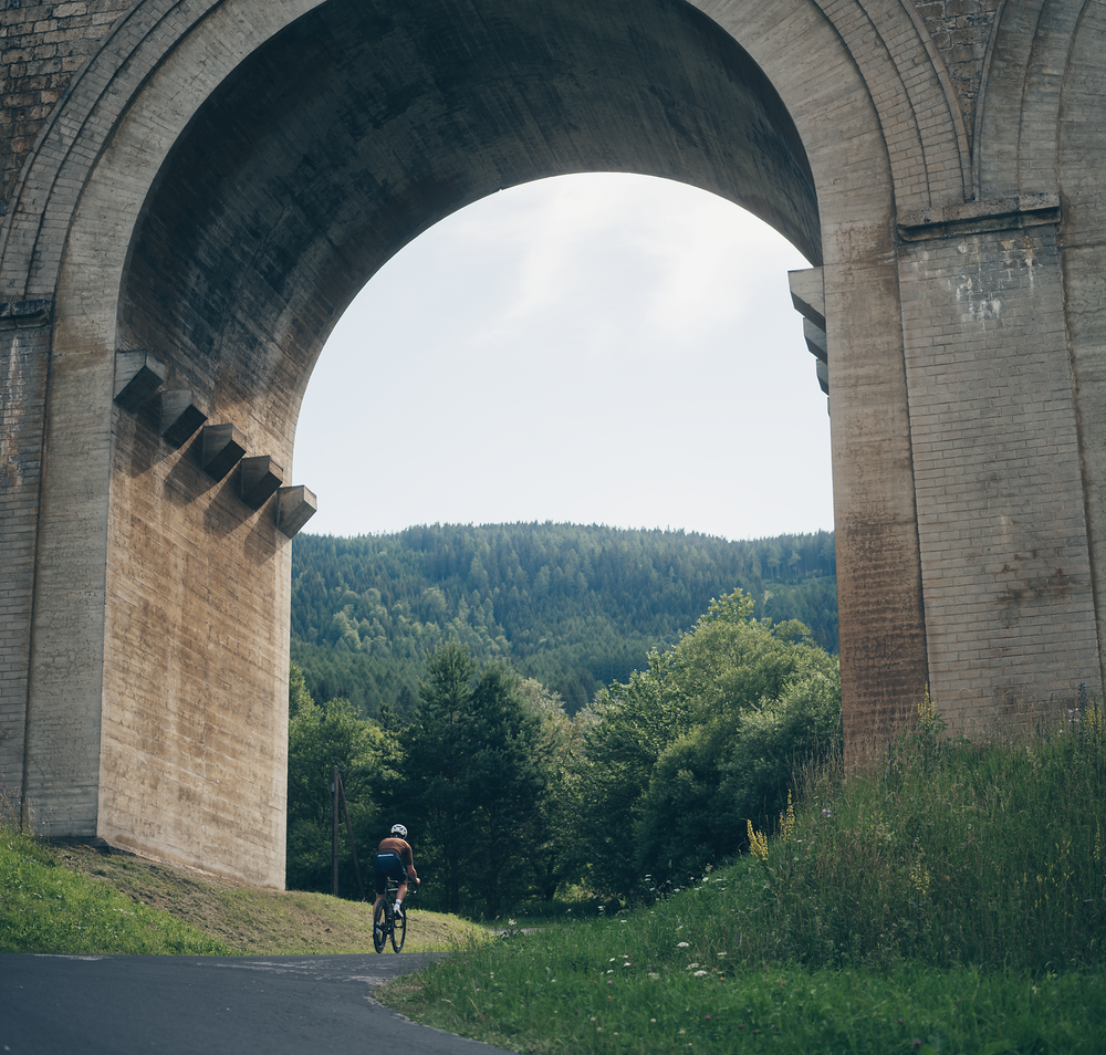 Unter majestätischen Bögen eines alten Viadukts radelt ein Abenteurer durch die grüne Landschaft. Die sanften Hügel und dichten Wälder laden dazu ein, die Schönheit der Natur zu erkunden und die frische Bergluft zu genießen. Ein perfekter Ort für unvergessliche Erlebnisse in den Wiener Alpen.