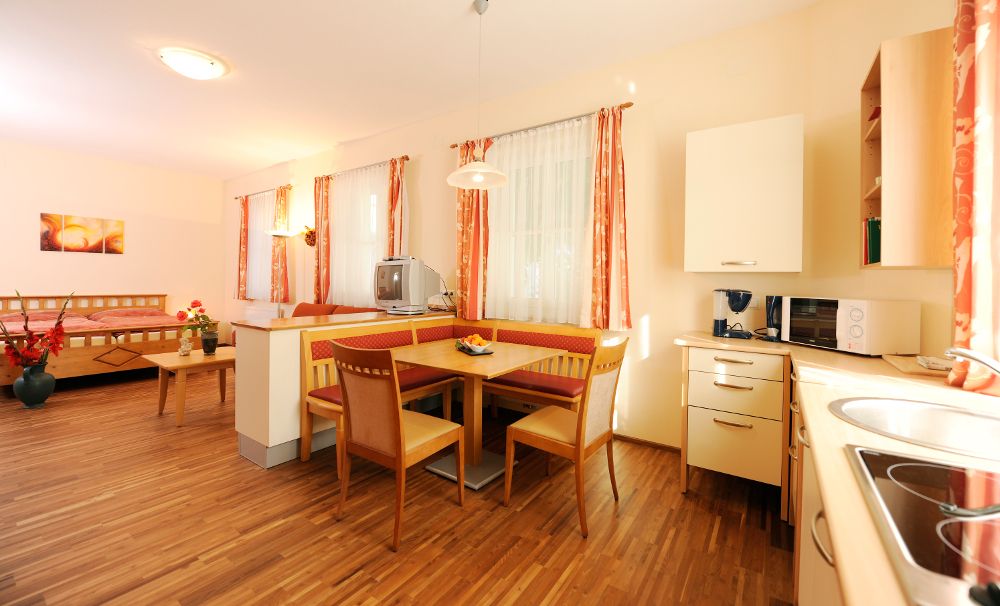 Helles Zimmer mit Holzboden, Esstisch, Küche und Bett.