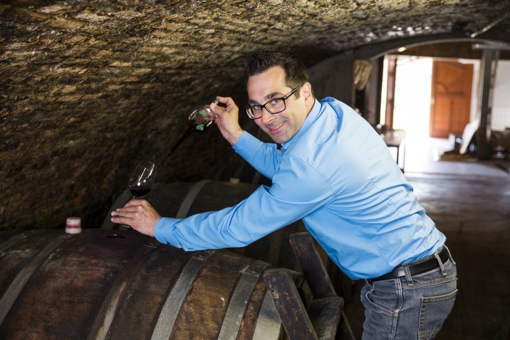 Mann in blauem Hemd zapft Wein aus einem Fass in einem Weinkeller.