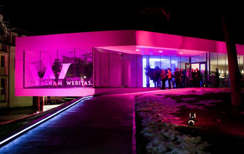 Moderne Vinothek bei Nacht mit pinker Beleuchtung und Menschen am Eingang.