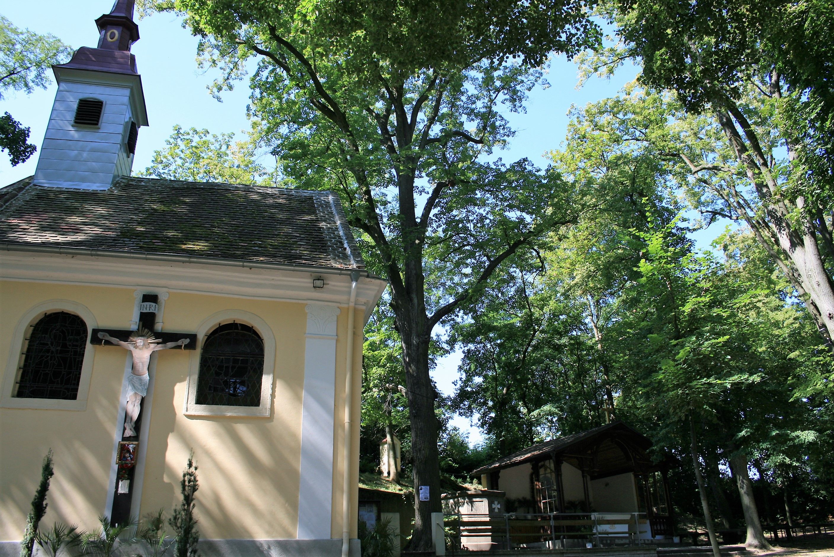 Eine kleine Kapelle im Wald mit einem Kruzifix an der Außenwand.