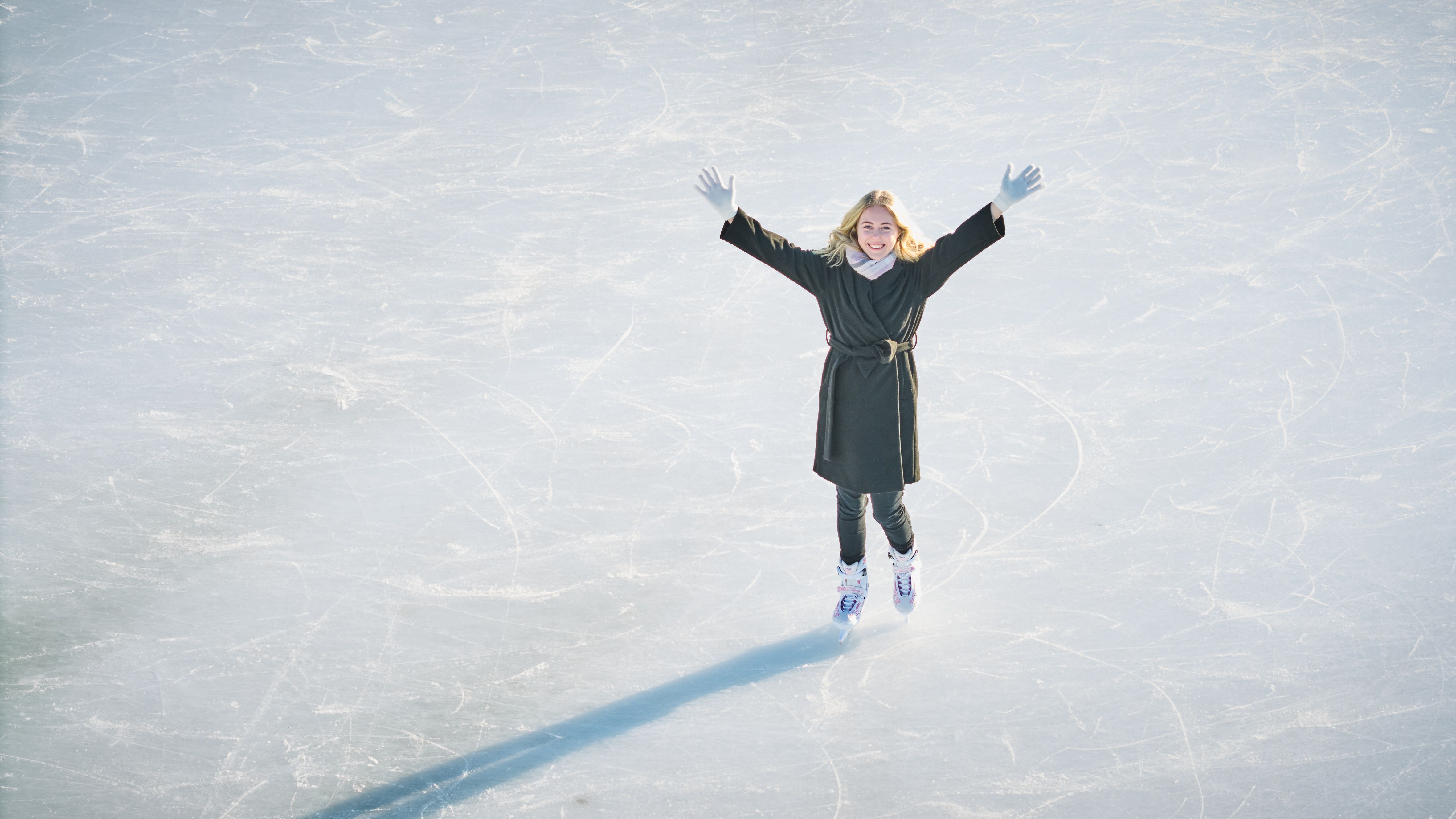 Person beim Eislaufen auf einer Eisfläche mit erhobenen Armen.
