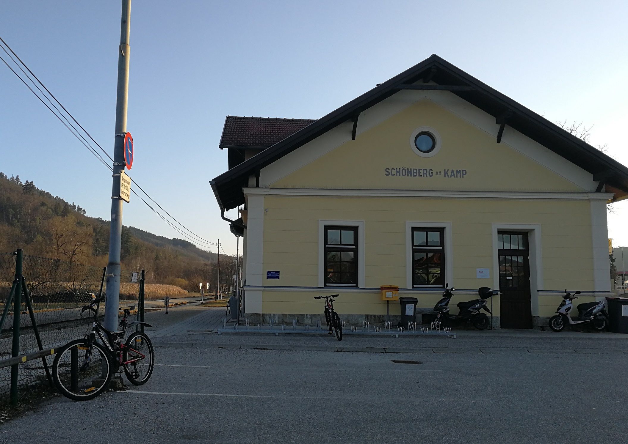 Bahnhof Schönberg am Kamp mit Fahrrädern und Rollern davor, umgeben von ländlicher Landschaft.