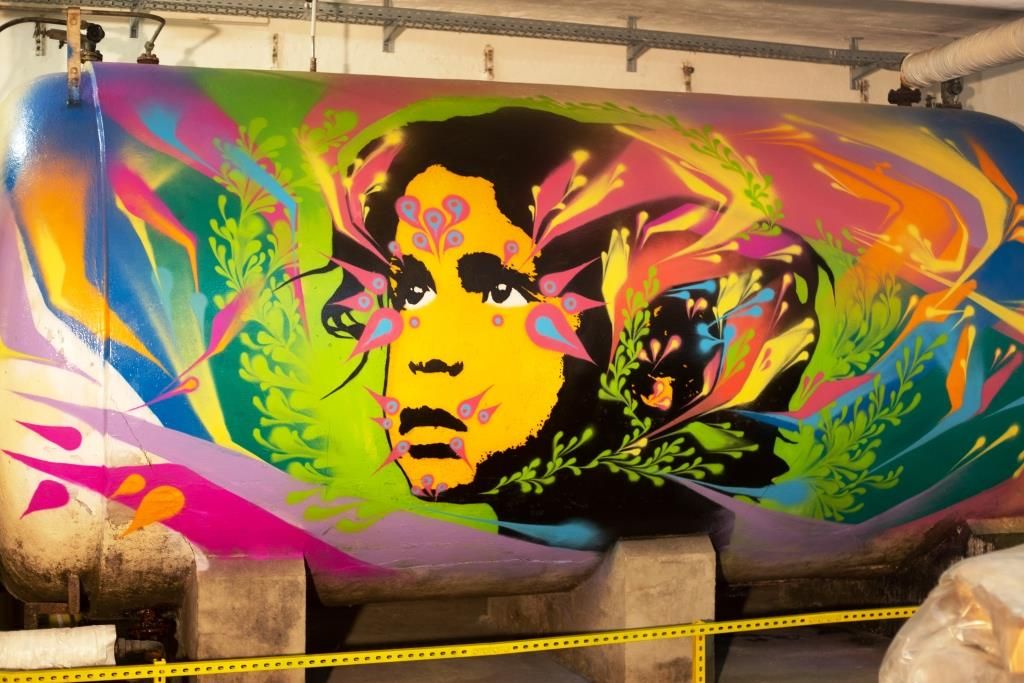 Graffiti auf einem Tank mit buntem Gesicht und Pflanzenmotiven.
