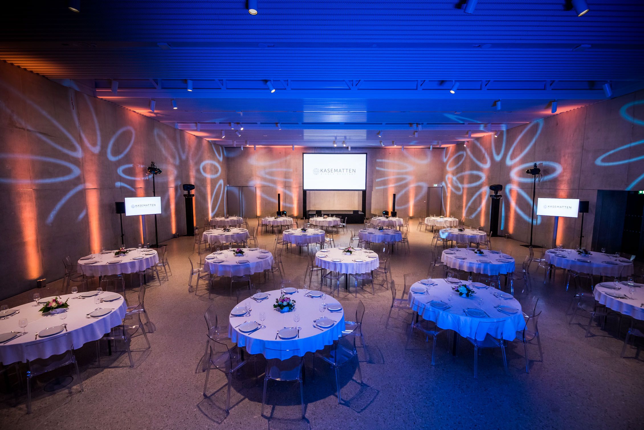 Ein eleganter Veranstaltungsraum mit runden, gedeckten Tischen und blauer Beleuchtung.